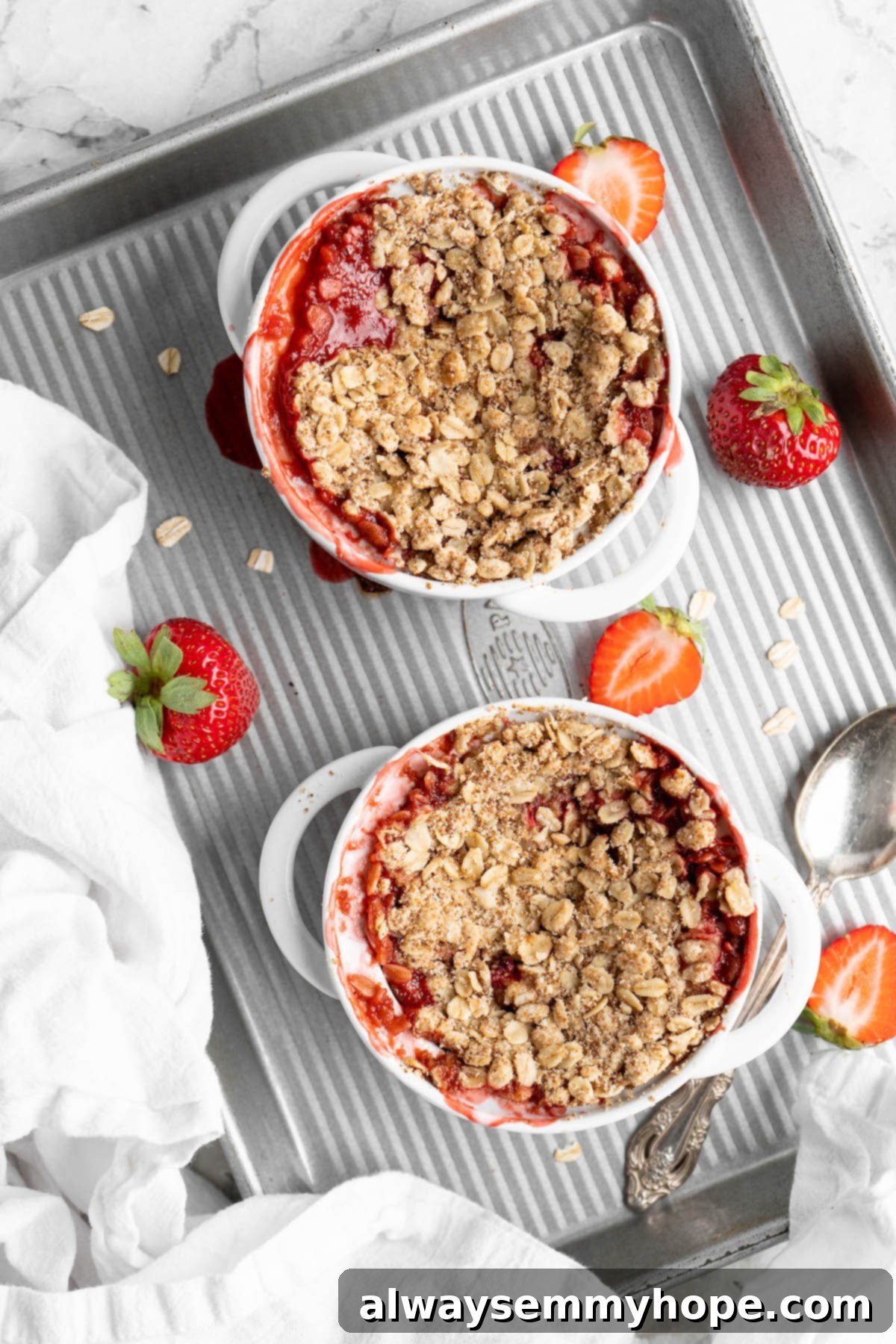 This vegan strawberry crumble is easy as can be! You only need 5 ingredients and a few minutes of assembly for the perfect summer dessert. Overhead view of two strawberry crumbles in ramekins on half sheet pan