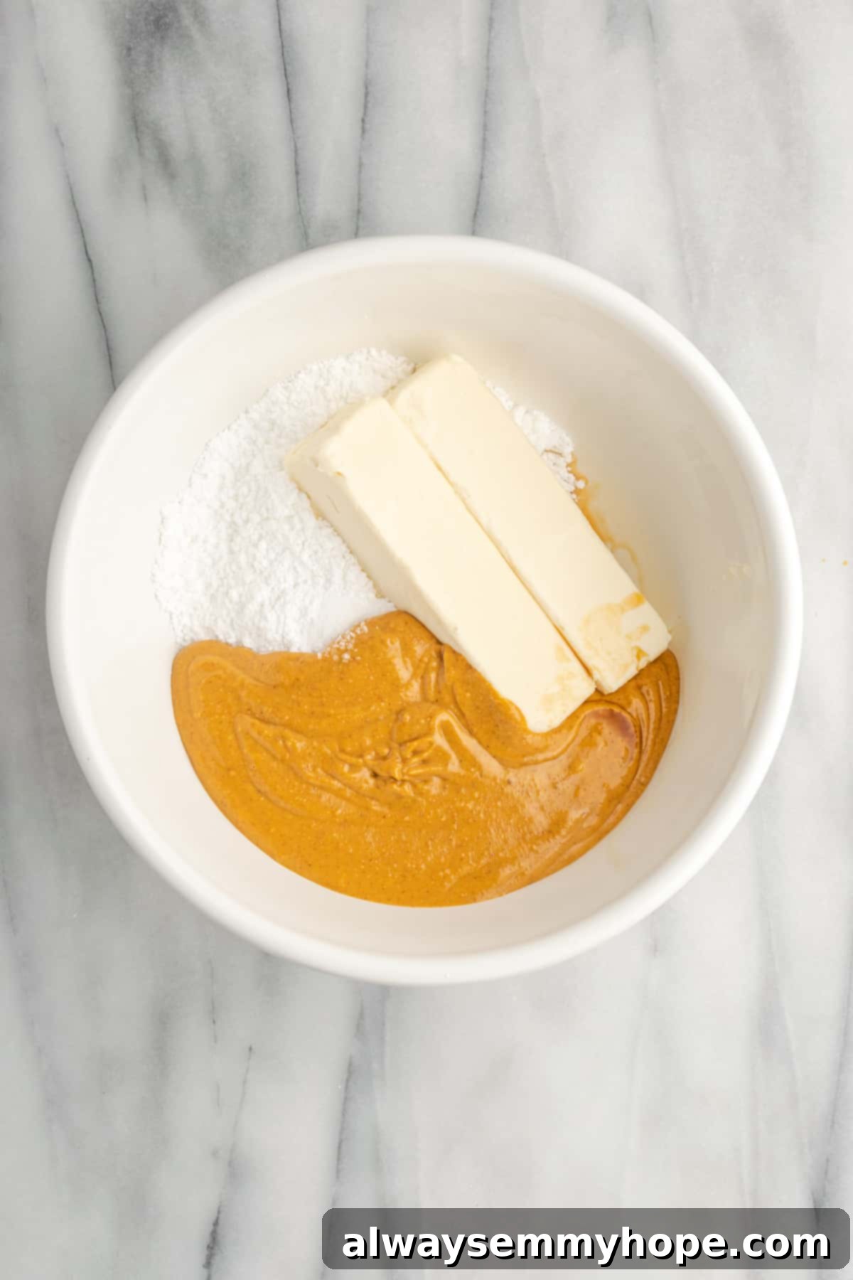A bowl filled with key frosting ingredients including softened vegan butter, smooth peanut butter, and confectioners' sugar, ready to be beaten into a creamy frosting.