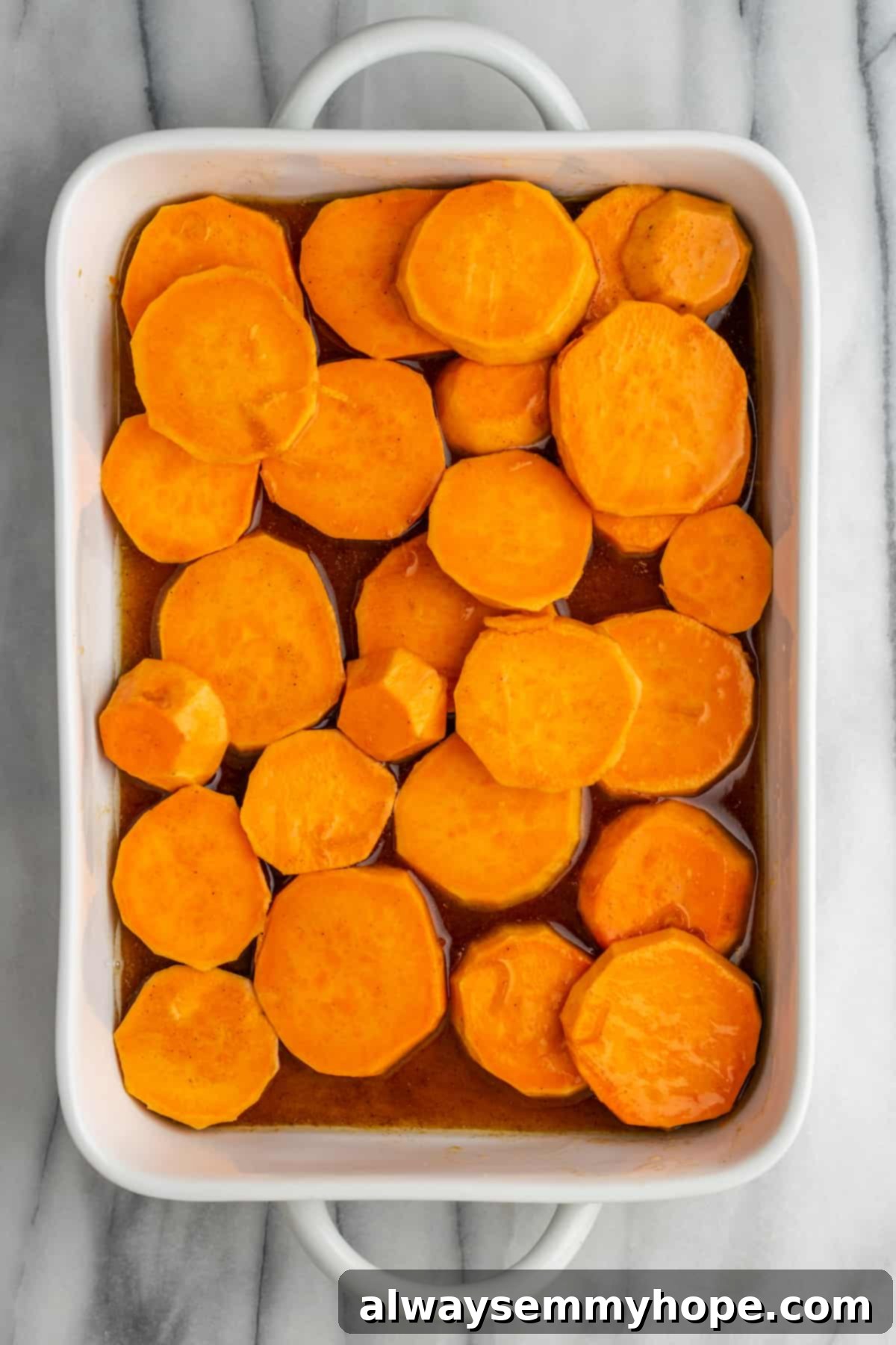 Uncooked yams in a baking tray, prepared for the sauce. Sliced raw yams arranged neatly in a glass baking tray, ready for the sauce.