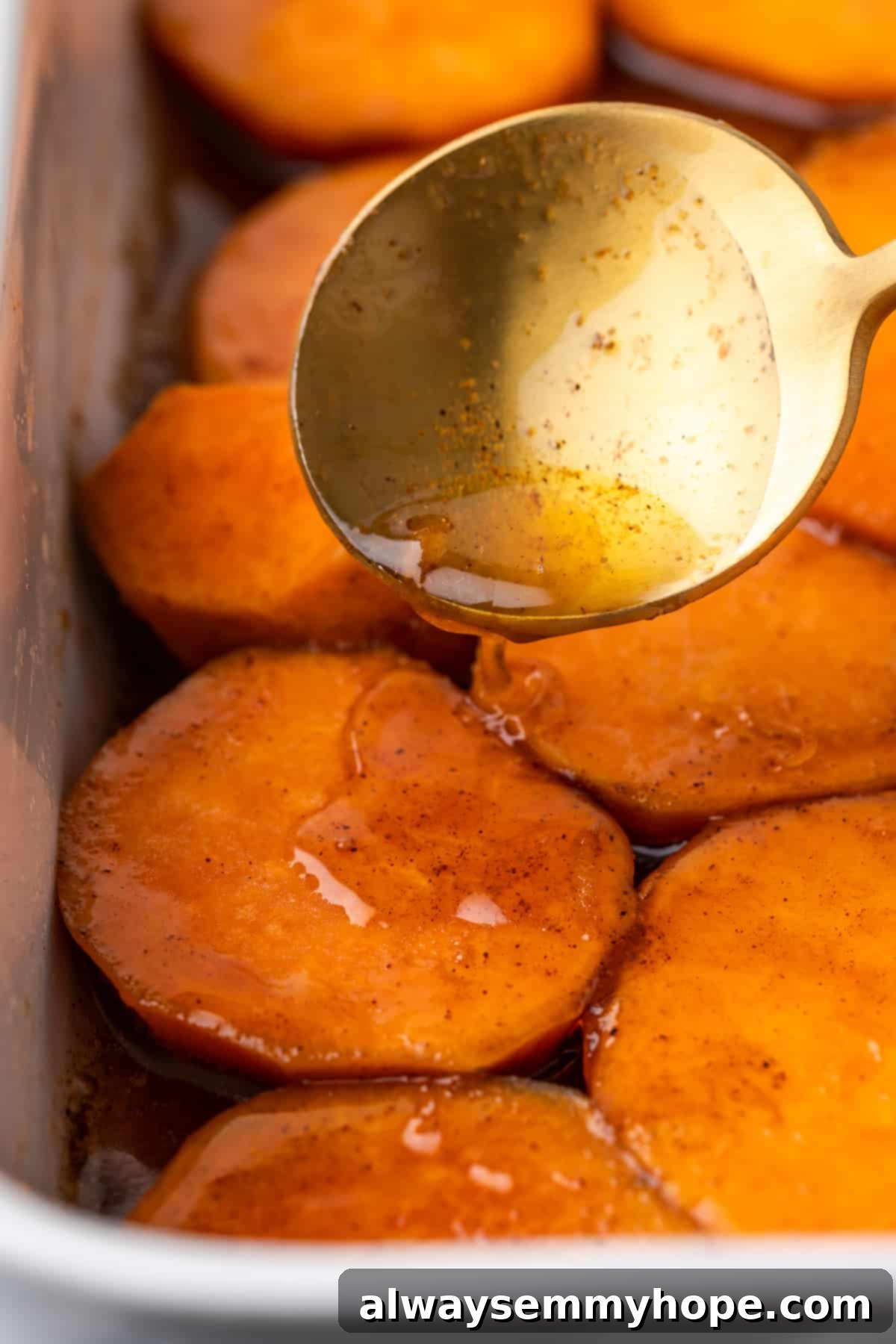 Spooning the sweet sauce over raw yams in a baking dish to coat them evenly. A large spoon pouring the amber-colored candied yam sauce over sliced yams in a baking dish.