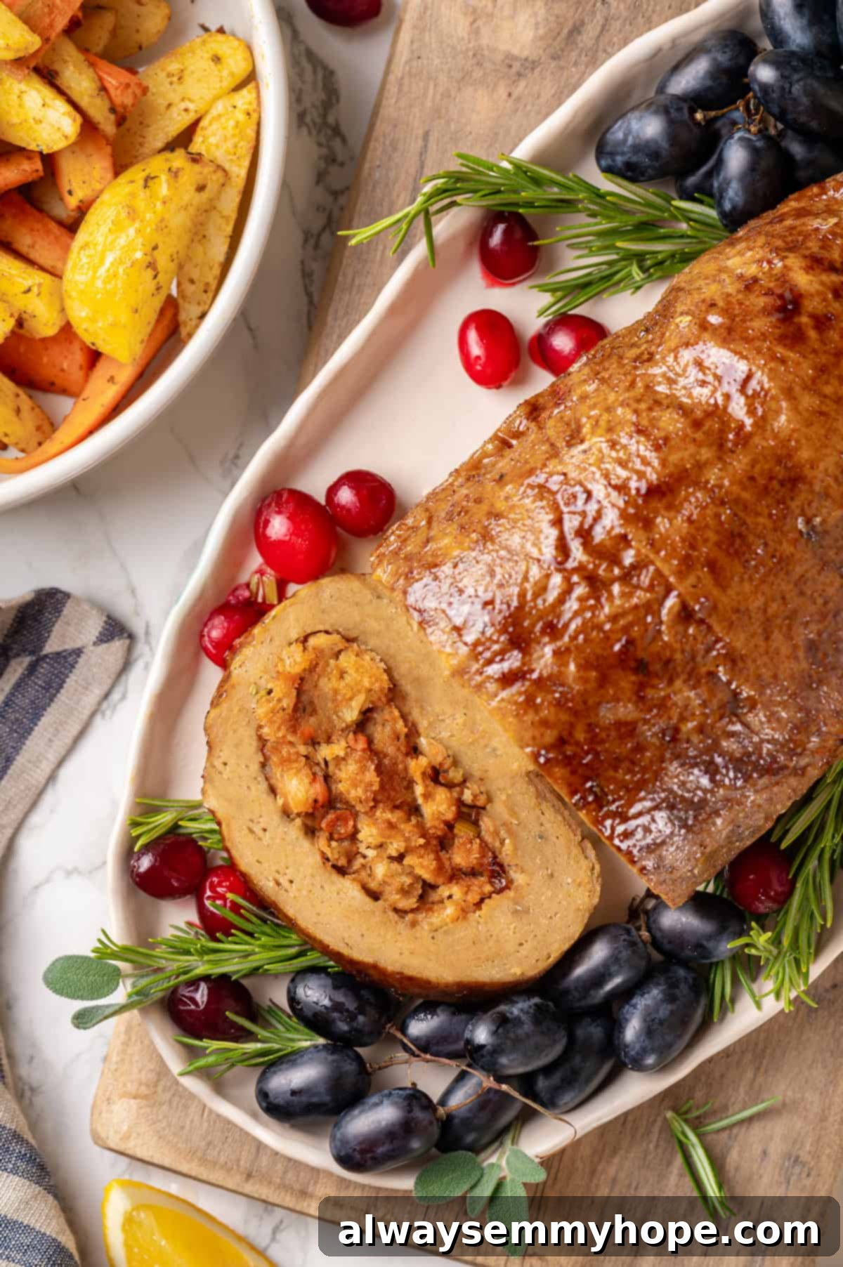 This homemade vegan turkey recipe is supremely flavourful and the perfect addition to any Thanksgiving table or holiday dinner! Overhead view of vegan turkey on platter with grapes and cranberries