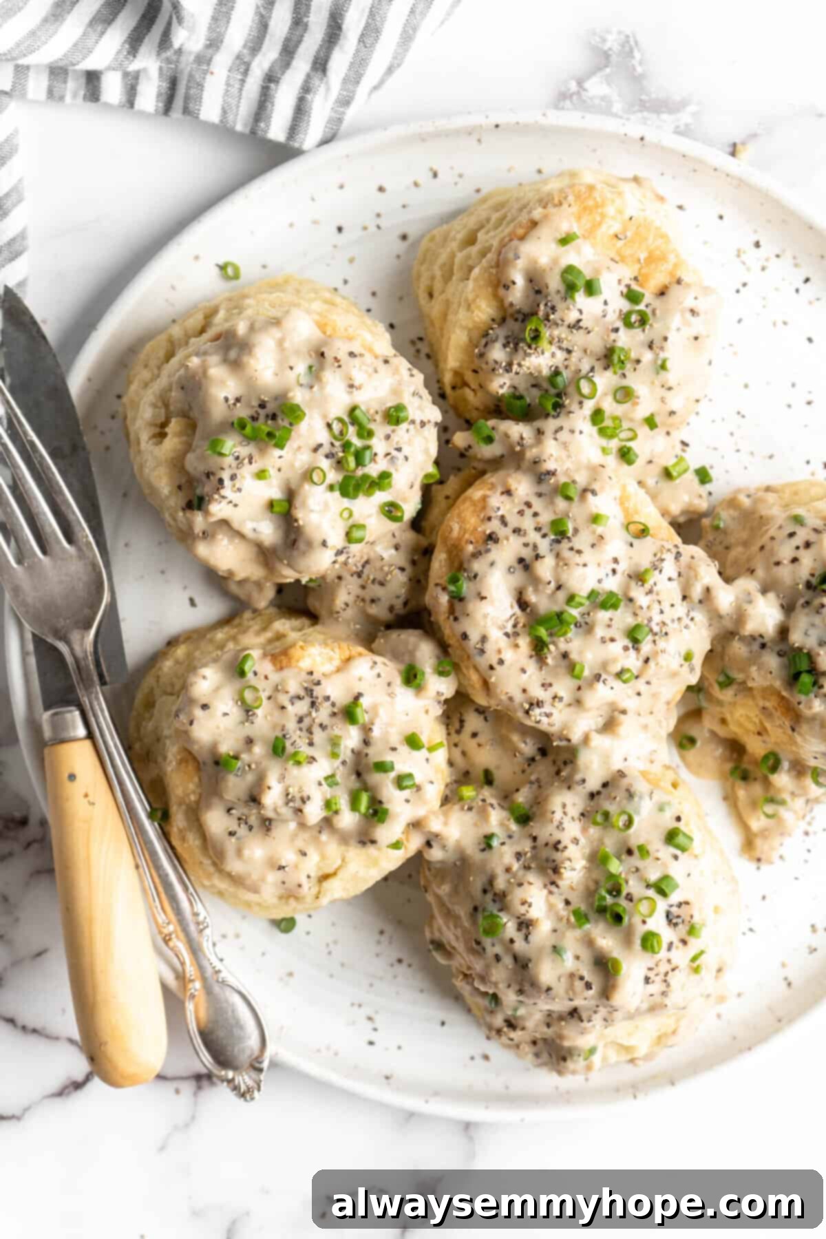 A plate with six biscuits covered in gravy and chives, with a fork and a knife
