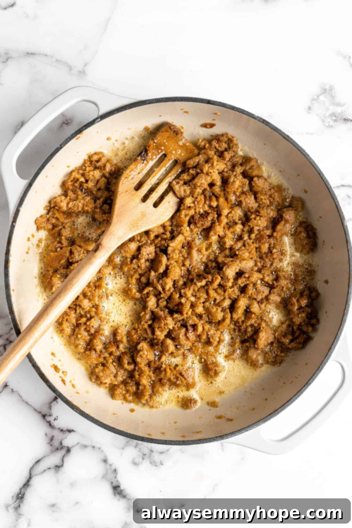 Vegan sausage cooking in a dutch oven with a slotted wooden spoon