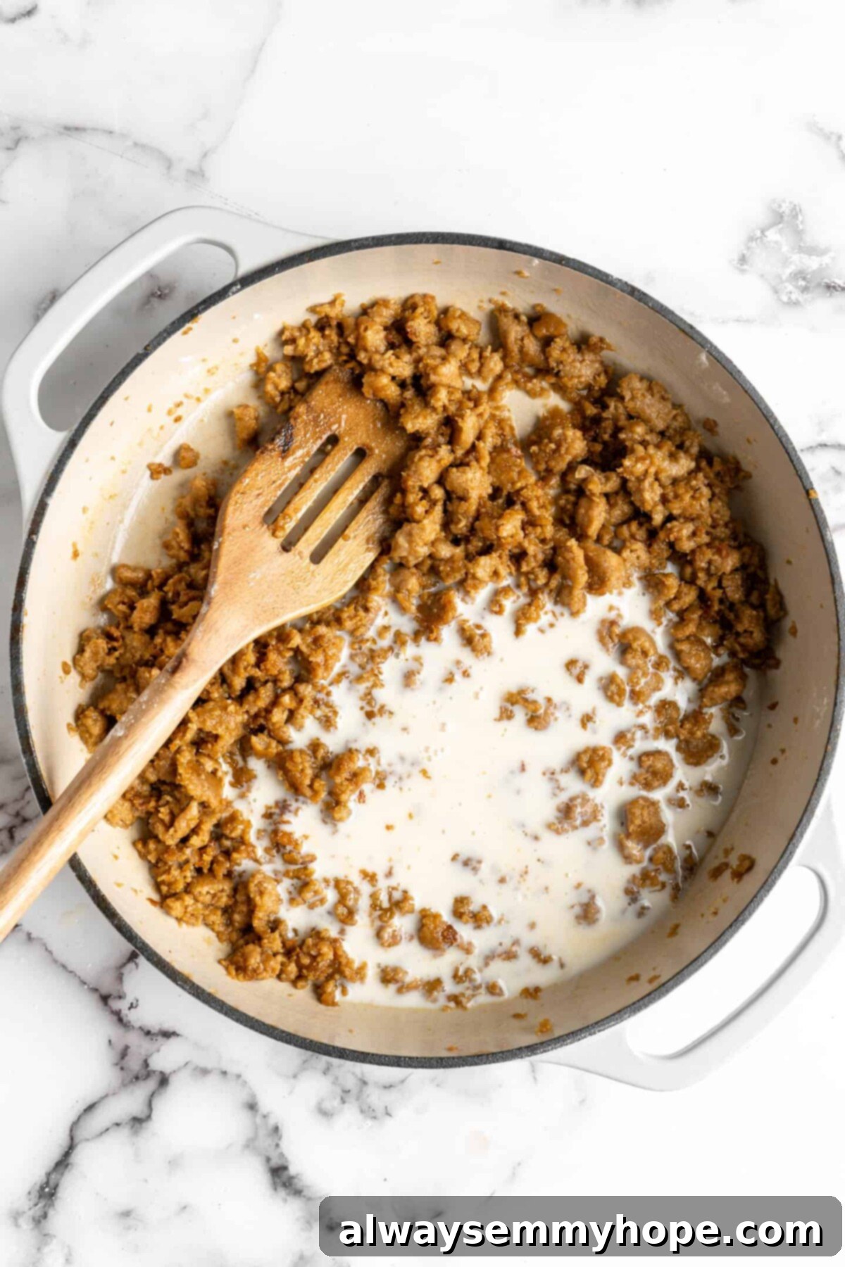 Cooked vegan sausage and a little bit of milk in a dutch oven with a slotted wooden spoon
