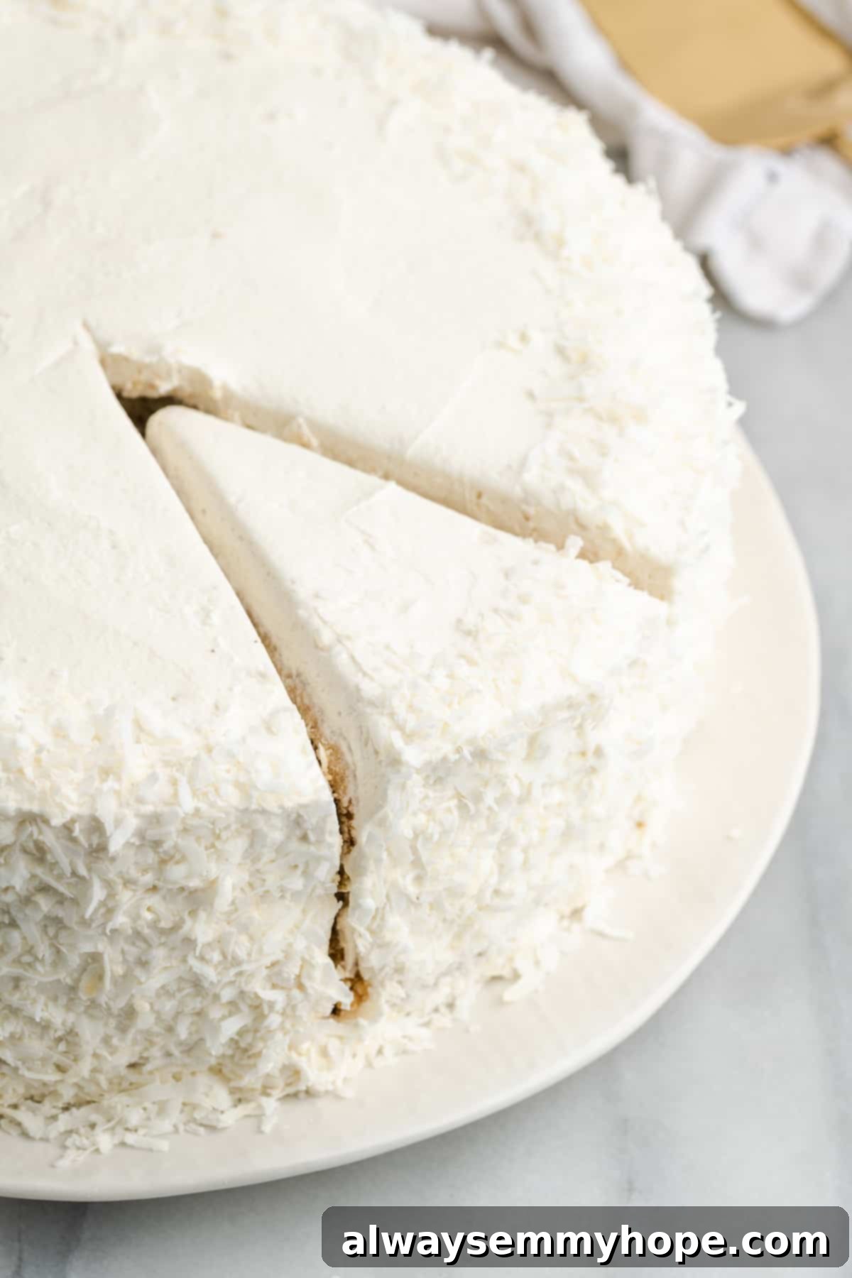 Tropical Vegan Coconut Cake 17 A complete vegan coconut cake, beautifully frosted and garnished with coconut flakes, with one perfect slice removed.