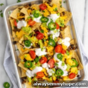 Epic Plant-Powered Nachos 2 Overhead view of a tray of nachos covered in vegan sour cream, tomatoes, and jalapeños