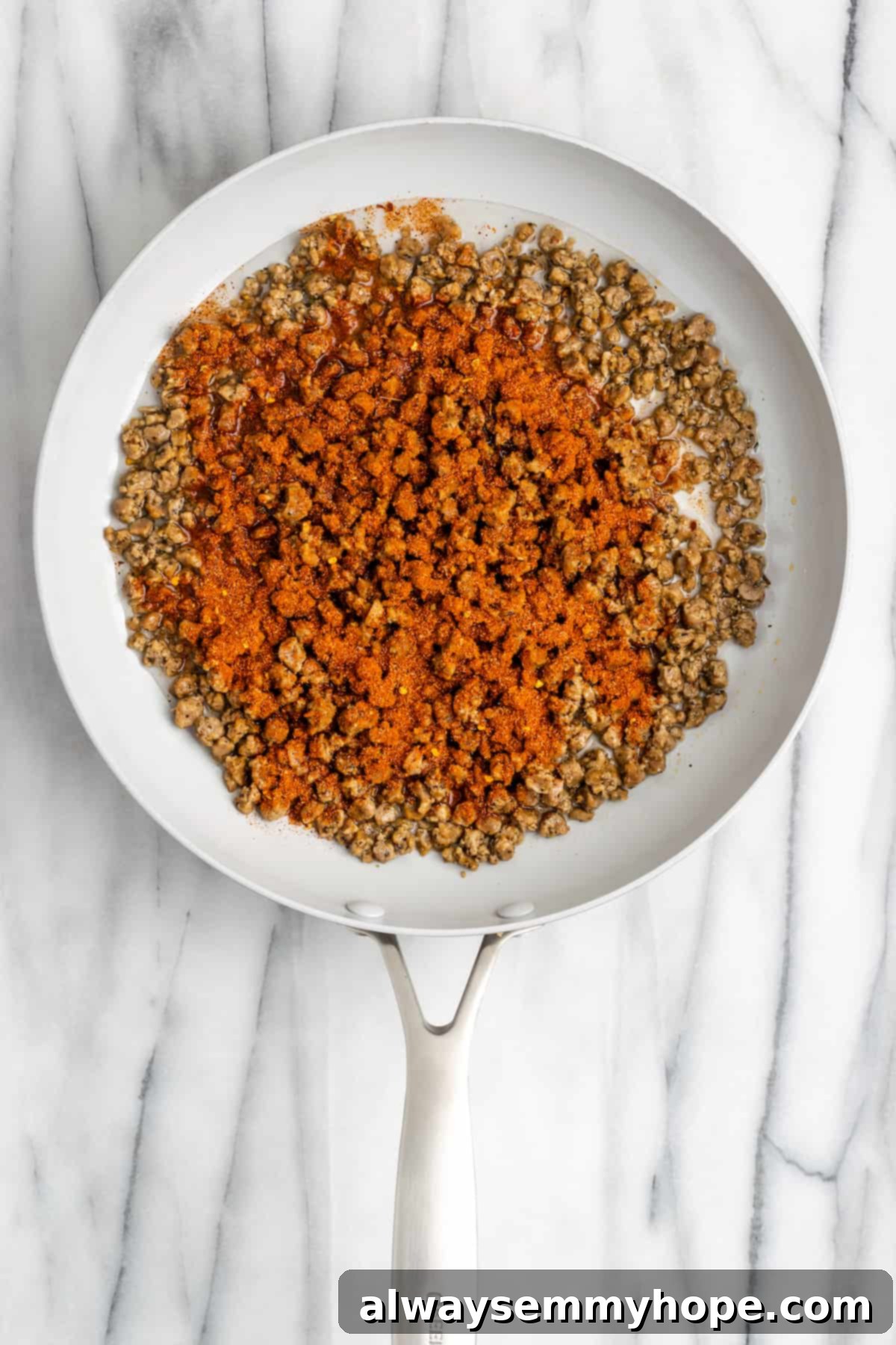 These vegan loaded nachos are rich and filling, with a spicy vegan meat crumble, black beans, a gooey vegan cheese sauce, and toppings. Vegan meat crumbles cooking in a pan, covered in taco seasoning.