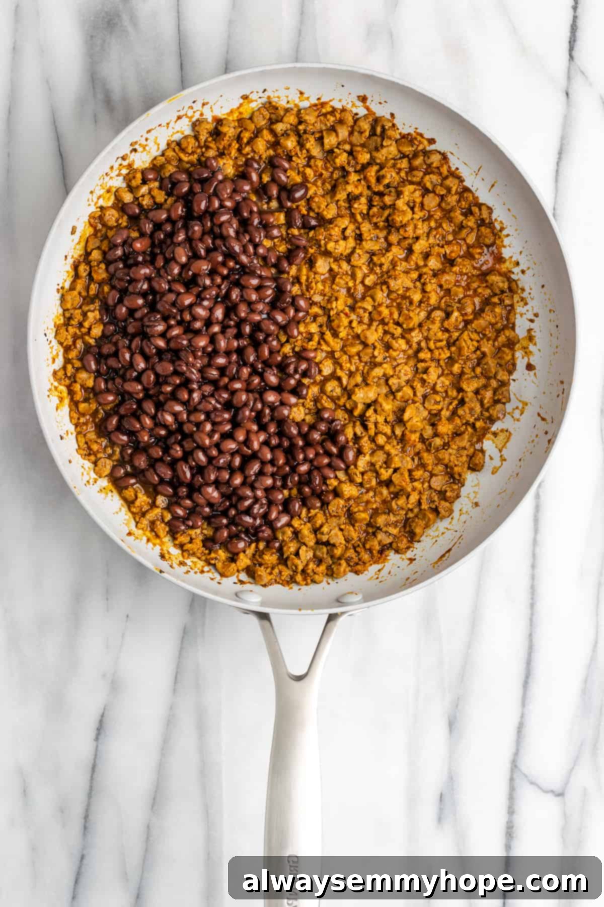 These vegan loaded nachos are rich and filling, with a spicy vegan meat crumble, black beans, a gooey vegan cheese sauce, and toppings. A pan with vegan meat crumbles and taco seasoning, with black beans poured on top.