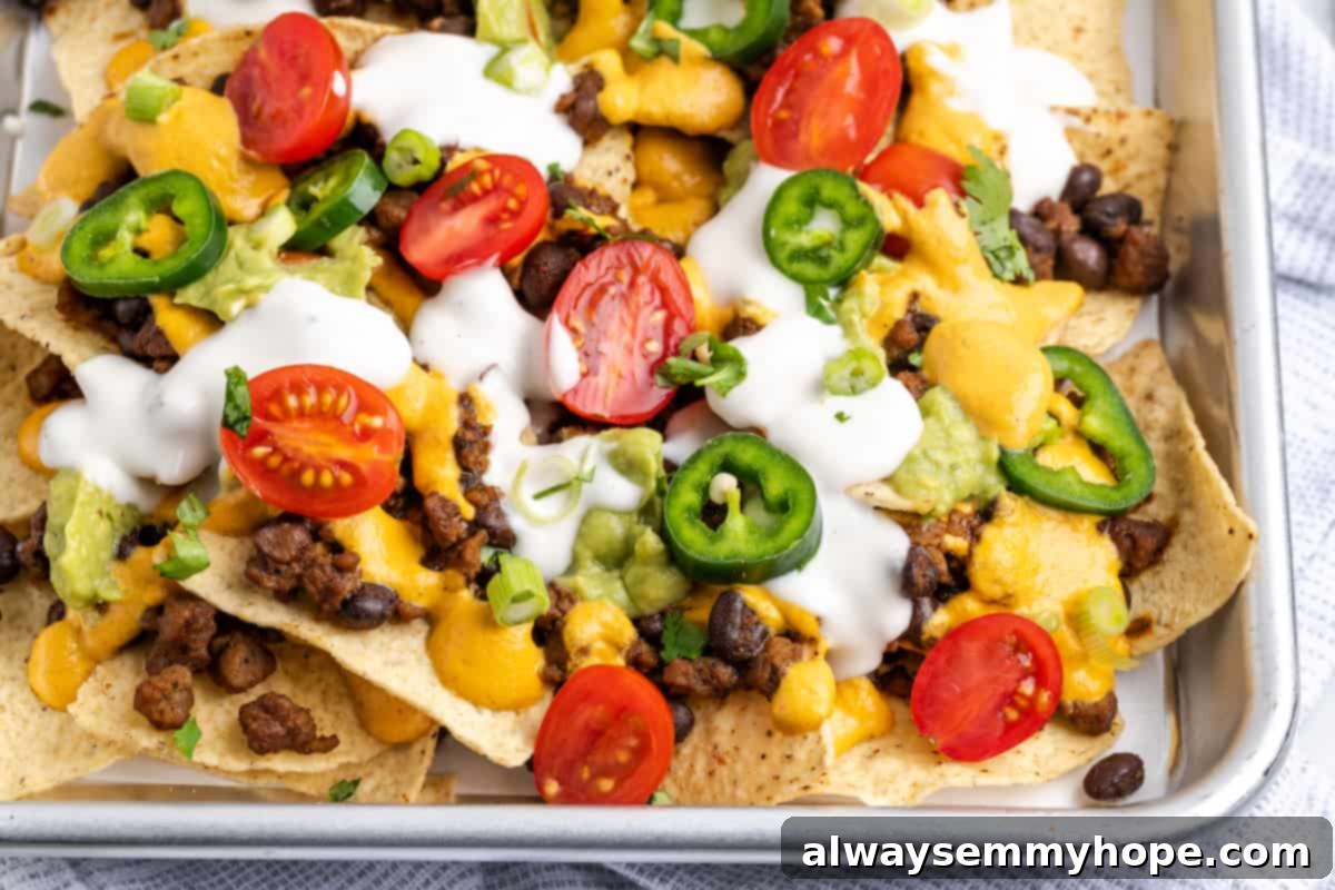 These vegan loaded nachos are rich and filling, with a spicy vegan meat crumble, black beans, a gooey vegan cheese sauce, and toppings. Close up of loaded vegan nachos covered in tomatoes, jalapeños, and vegan sour cream.