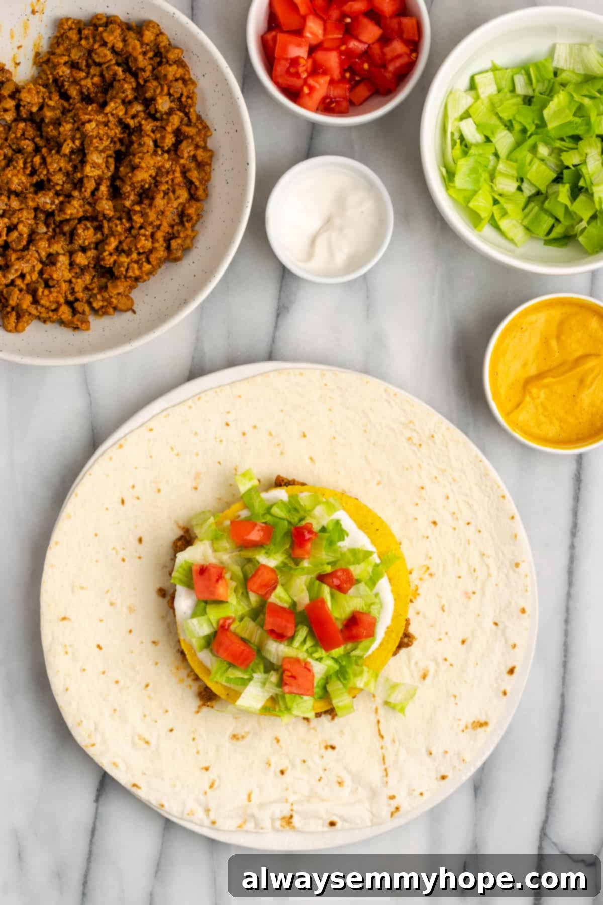 A fully loaded tortilla, featuring all layers: vegan meat, cheese, tostada, sour cream, lettuce, and diced tomatoes, ready for folding. This visually appealing stack is packed with flavor.