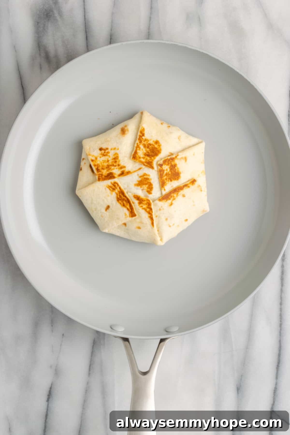 A vegan crunchwrap supreme toasting in a non-stick skillet, achieving a golden-brown, crispy exterior. The seams are sealed, and the wrap looks perfectly cooked.