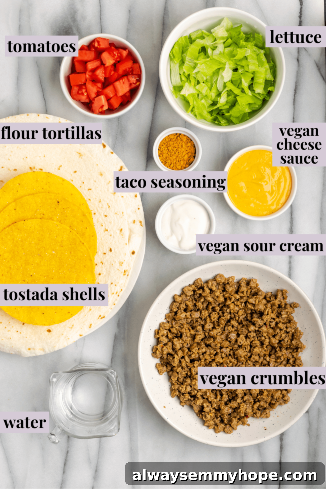 Overhead view of the ingredients for vegan crunchwrap supremes: large flour tortillas, crispy tostada shells, a bowl of seasoned vegan meat crumbles, a bowl of shredded lettuce, a bowl of diced tomatoes, a bowl of taco seasoning, a bowl of creamy vegan sour cream, a bowl of golden vegan cheese sauce, and a glass of water.