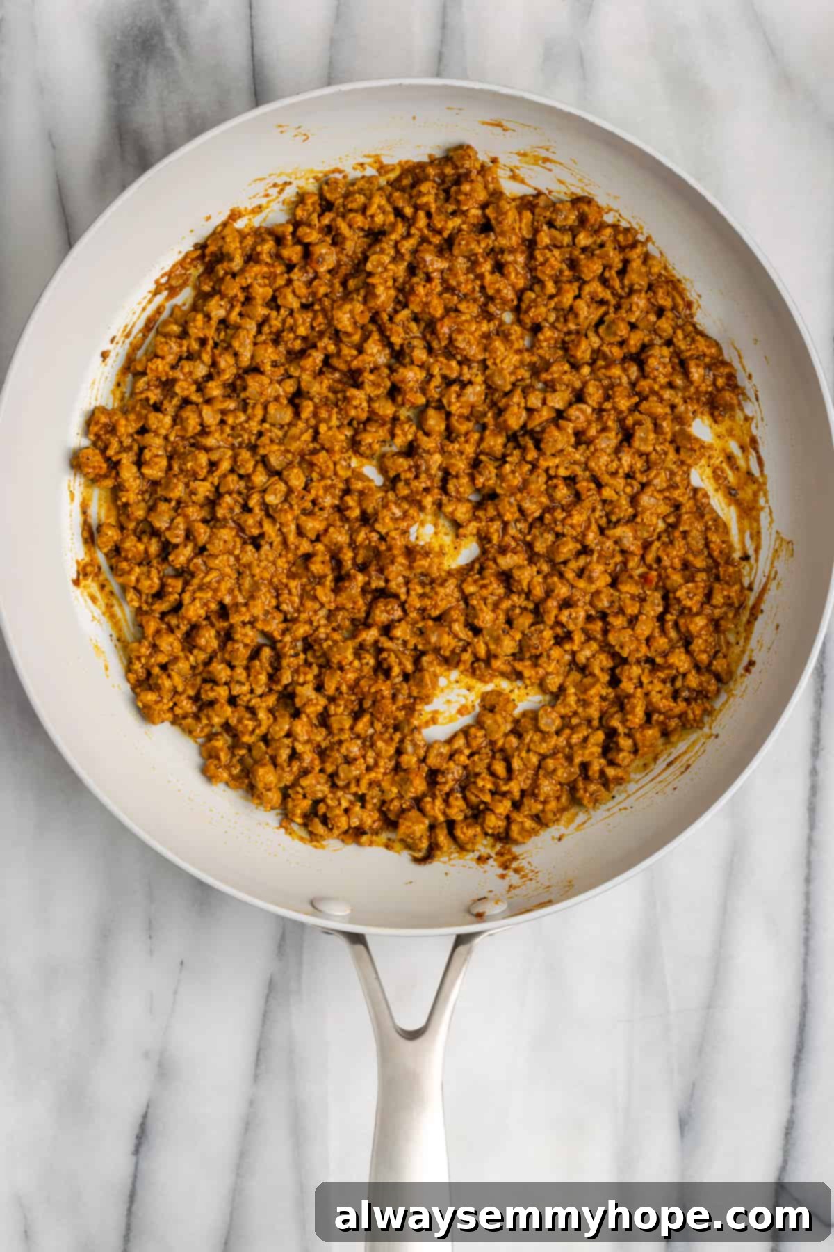 Vegan meat crumbles cooking in a pan with taco seasoning and water, bubbling and absorbing the liquid. The mixture is savory and aromatic.