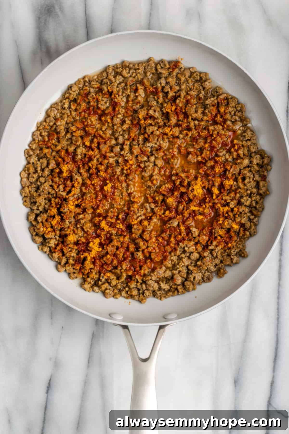 Vegan meat crumbles cooking in a pan with taco seasoning, now mostly dry and well-seasoned, ready for assembly. The crumbles are evenly coated and fragrant.