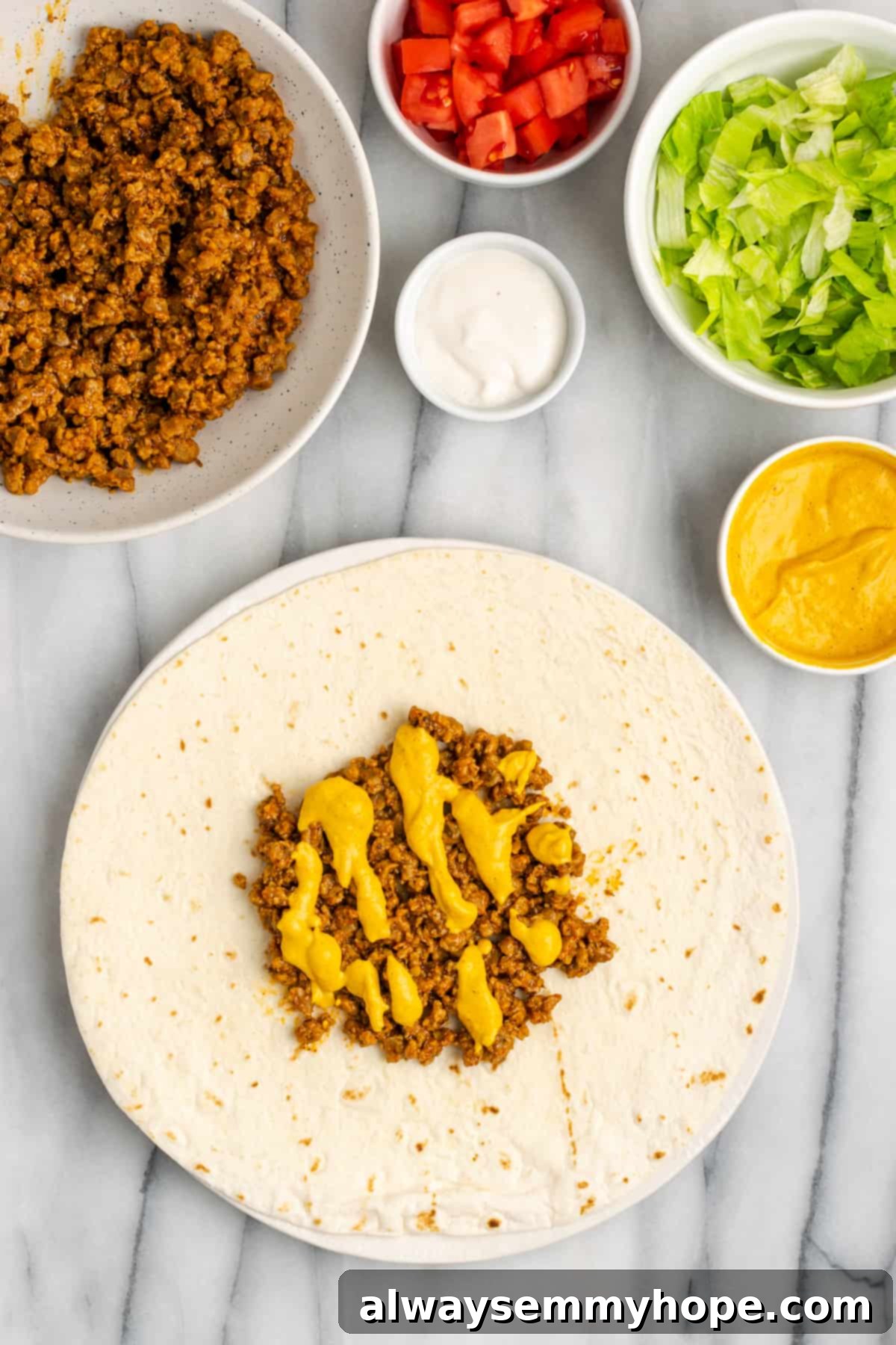 A flour tortilla topped with vegan meat crumbles and a luscious drizzle of golden vegan cheese sauce, creating a rich and gooey layer. Other ingredients are neatly arranged around it.