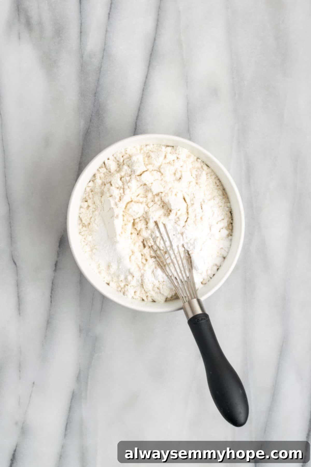 This buttery vegan spritz cookies recipe is fun to make and eat, and the cookies are moist, tender, and full of almond and vanilla flavor. A small bowl with flour, tapioca starch, and salt, mixed together, with a whisk in it, ready for the next step