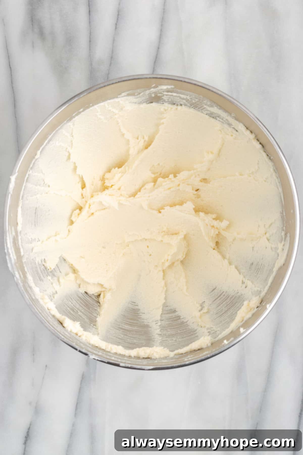 This buttery vegan spritz cookies recipe is fun to make and eat, and the cookies are moist, tender, and full of almond and vanilla flavor. A mixing bowl with beaten vegan butter and sugar in it, showcasing the creamy, light texture