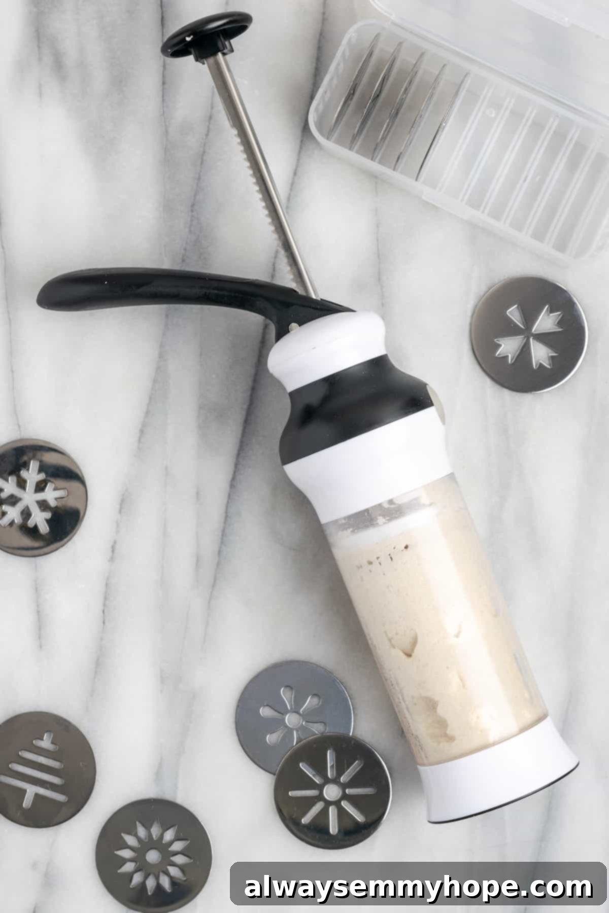 This buttery vegan spritz cookies recipe is fun to make and eat, and the cookies are moist, tender, and full of almond and vanilla flavor. A spritz gun filled with cookie dough, with various tips surrounding it, demonstrating the tool in action