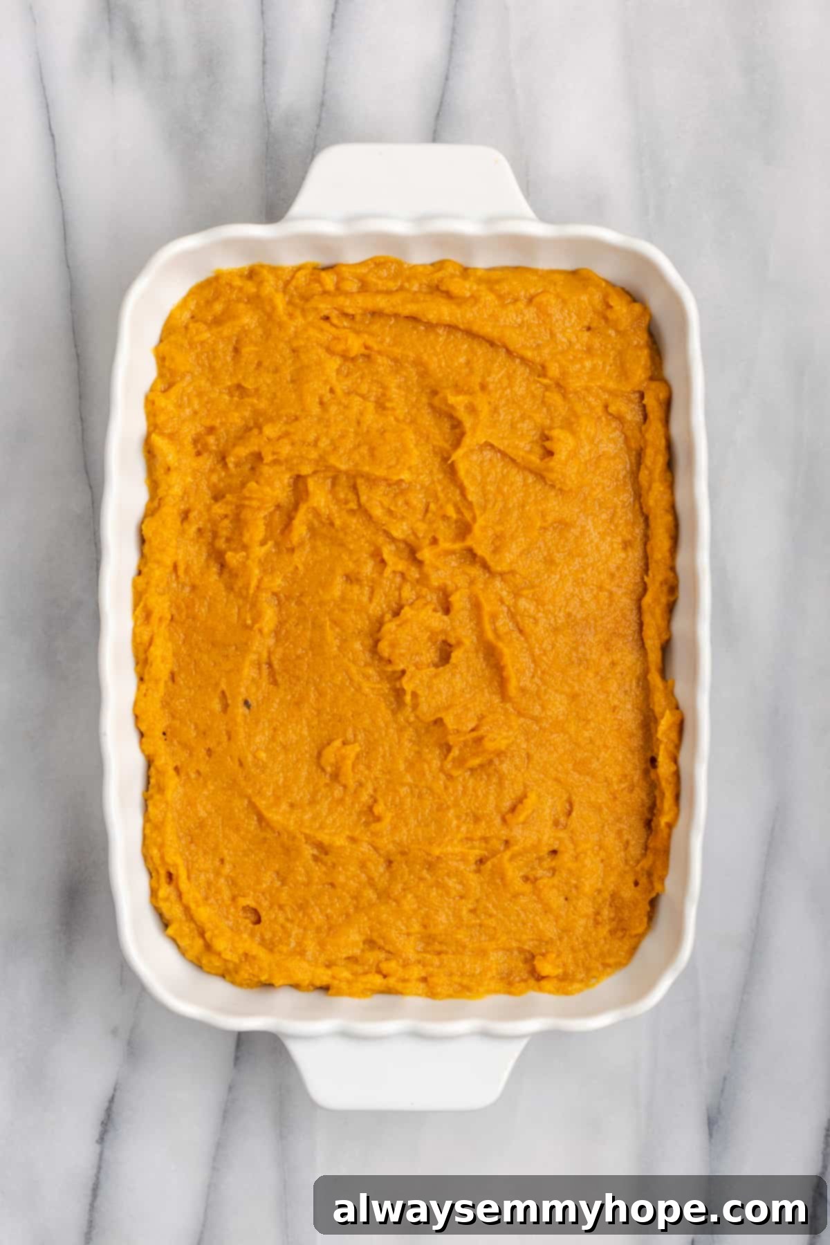 This rich and creamy vegan sweet potato soufflé recipe is a cozy Thanksgiving side. It's entirely vegan, and can easily be made gluten-free. An overhead view of the uncooked sweet potato soufflé batter, spread smoothly and evenly in a casserole dish, ready for its topping.