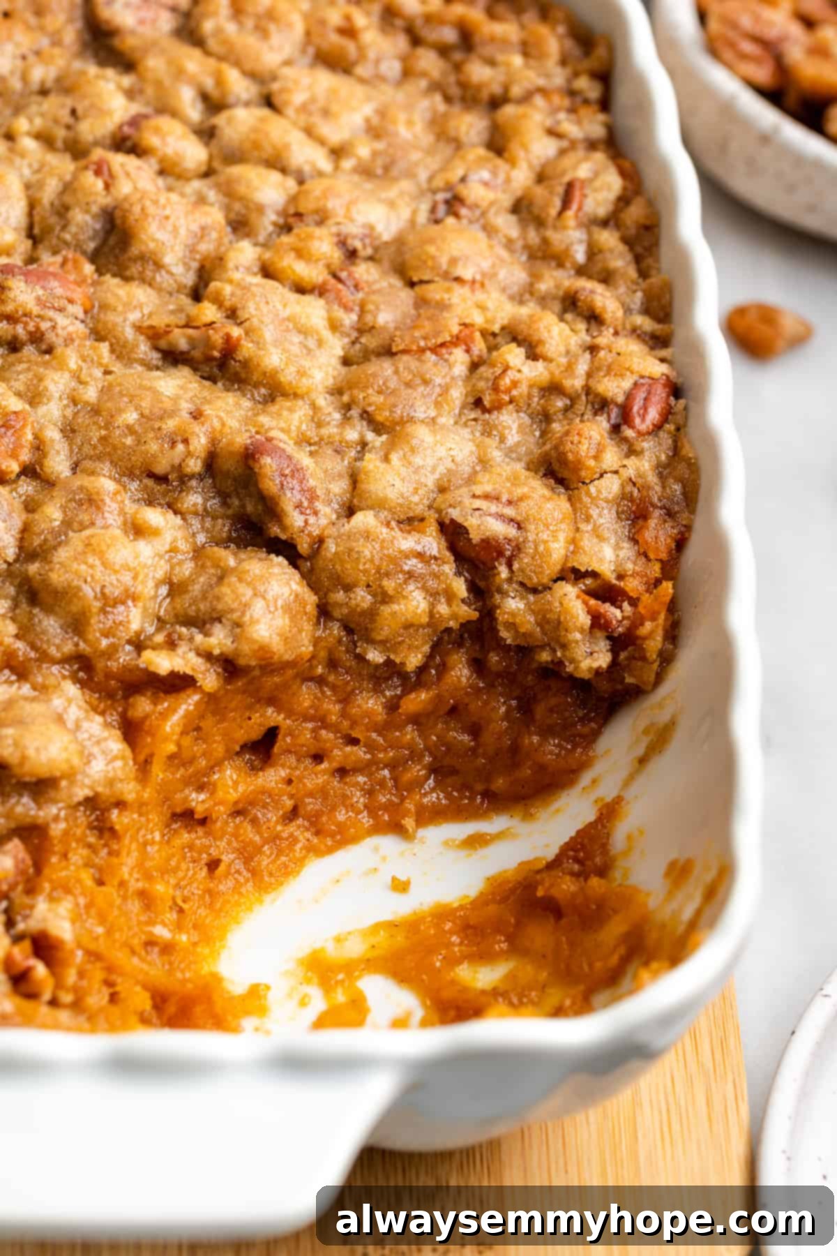 This rich and creamy vegan sweet potato soufflé recipe is a cozy Thanksgiving side. It's entirely vegan, and can easily be made gluten-free. A freshly baked sweet potato soufflé in a casserole dish, with a single corner serving beautifully removed, revealing its creamy interior and crisp pecan topping.