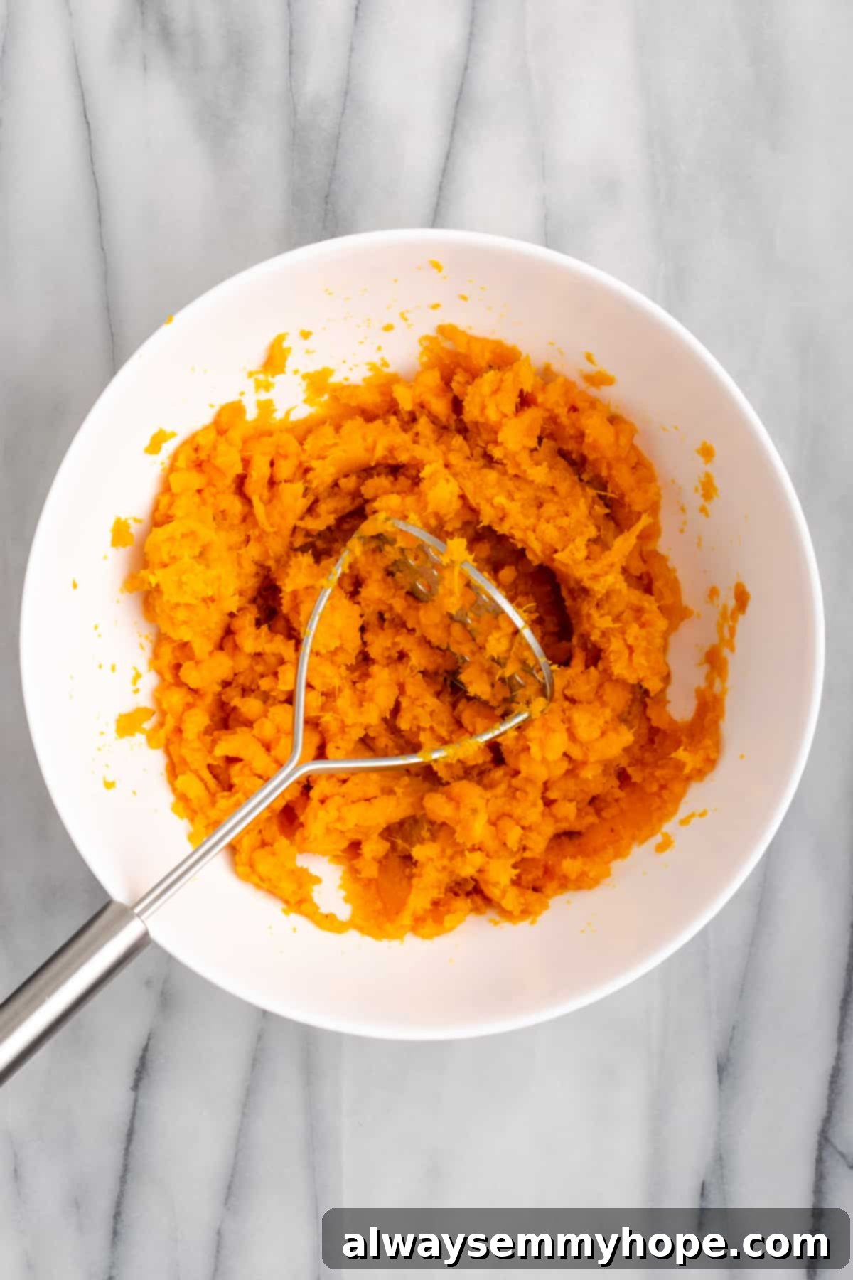 This rich and creamy vegan sweet potato soufflé recipe is a cozy Thanksgiving side. It's entirely vegan, and can easily be made gluten-free. A mixing bowl filled with smooth, mashed sweet potatoes, with a potato masher resting in the creamy mixture.