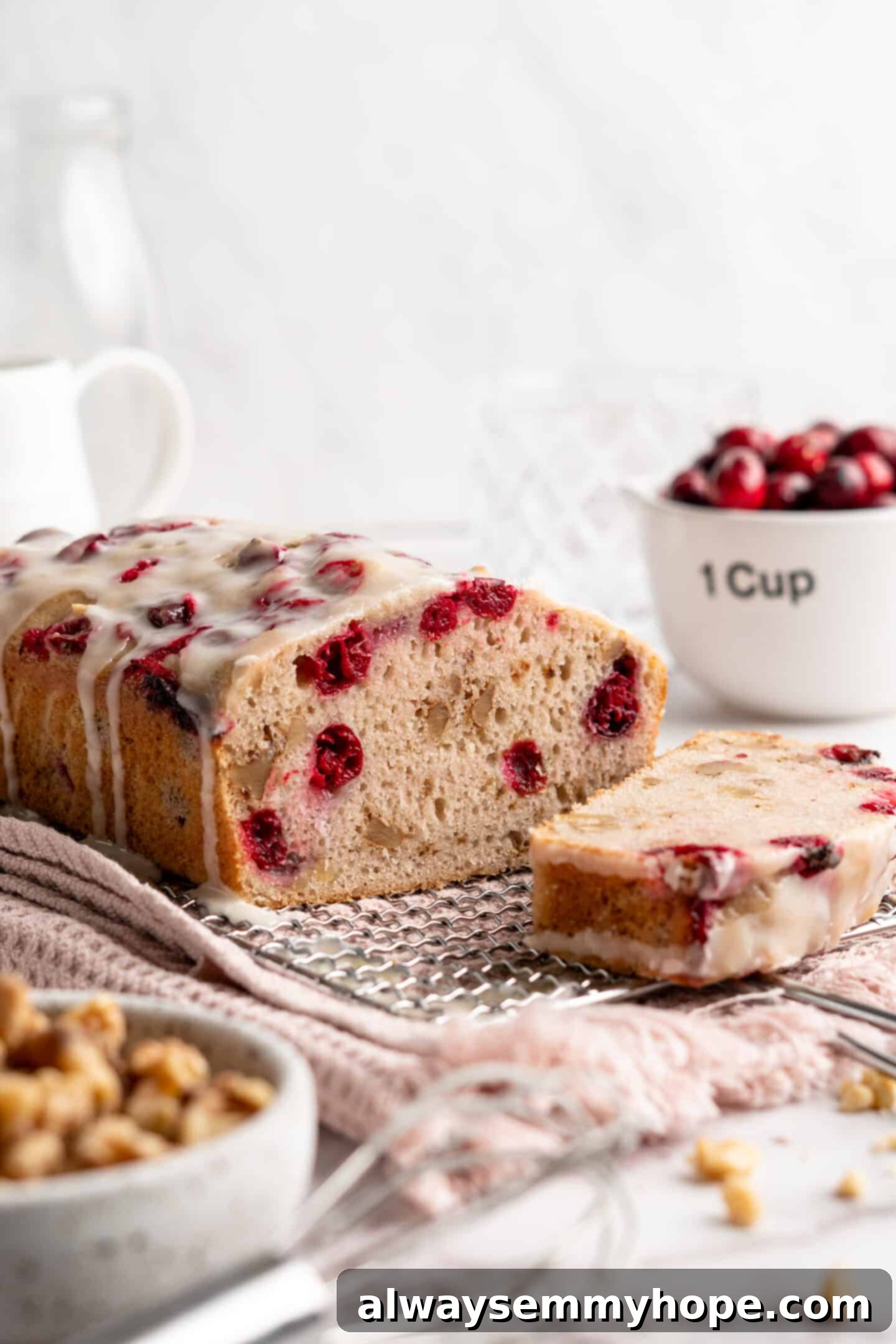 This moist cranberry walnut bread has just the right balance of sweetness, nuttiness, and tartness, and is a perfect holiday treat. A beautifully baked loaf of cranberry walnut bread on a cooling rack, freshly sliced to reveal its moist interior, with a separate slice presented in front and a bowl of fresh cranberries in the background.