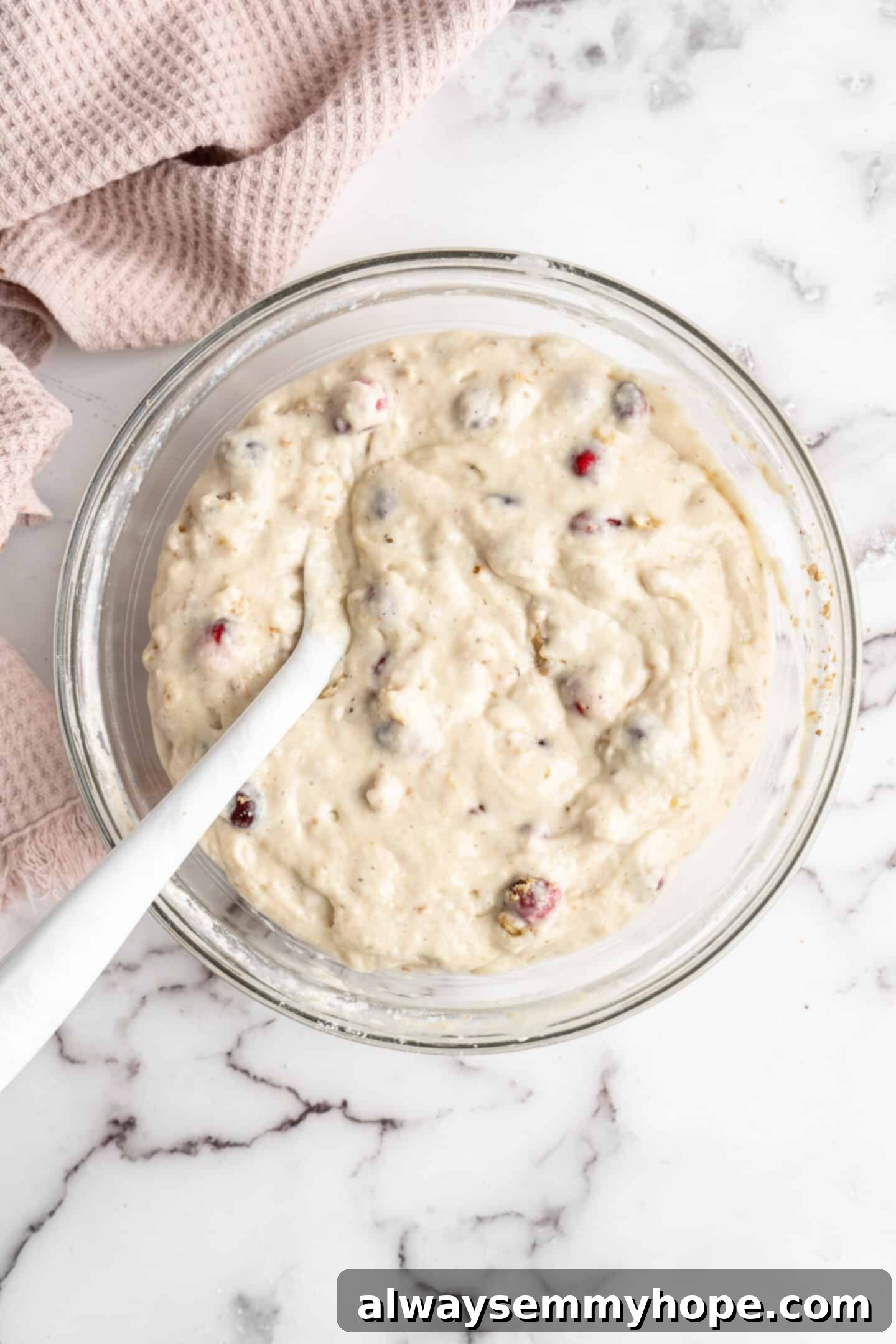 This moist cranberry walnut bread has just the right balance of sweetness, nuttiness, and tartness, and is a perfect holiday treat. A mixing bowl brimming with fully mixed cranberry walnut bread batter, showcasing the even distribution of cranberries and walnuts, with a rubber spatula resting inside.