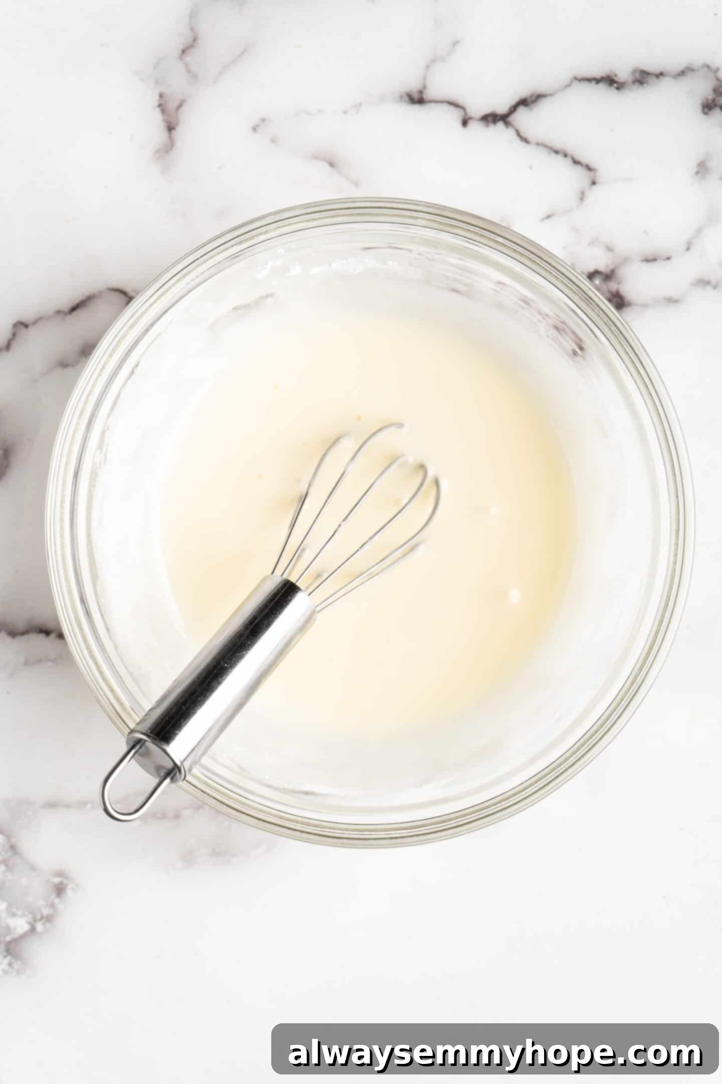 This moist cranberry walnut bread has just the right balance of sweetness, nuttiness, and tartness, and is a perfect holiday treat. A mixing bowl containing a smoothly blended orange glaze, with a whisk immersed, showcasing its creamy texture.