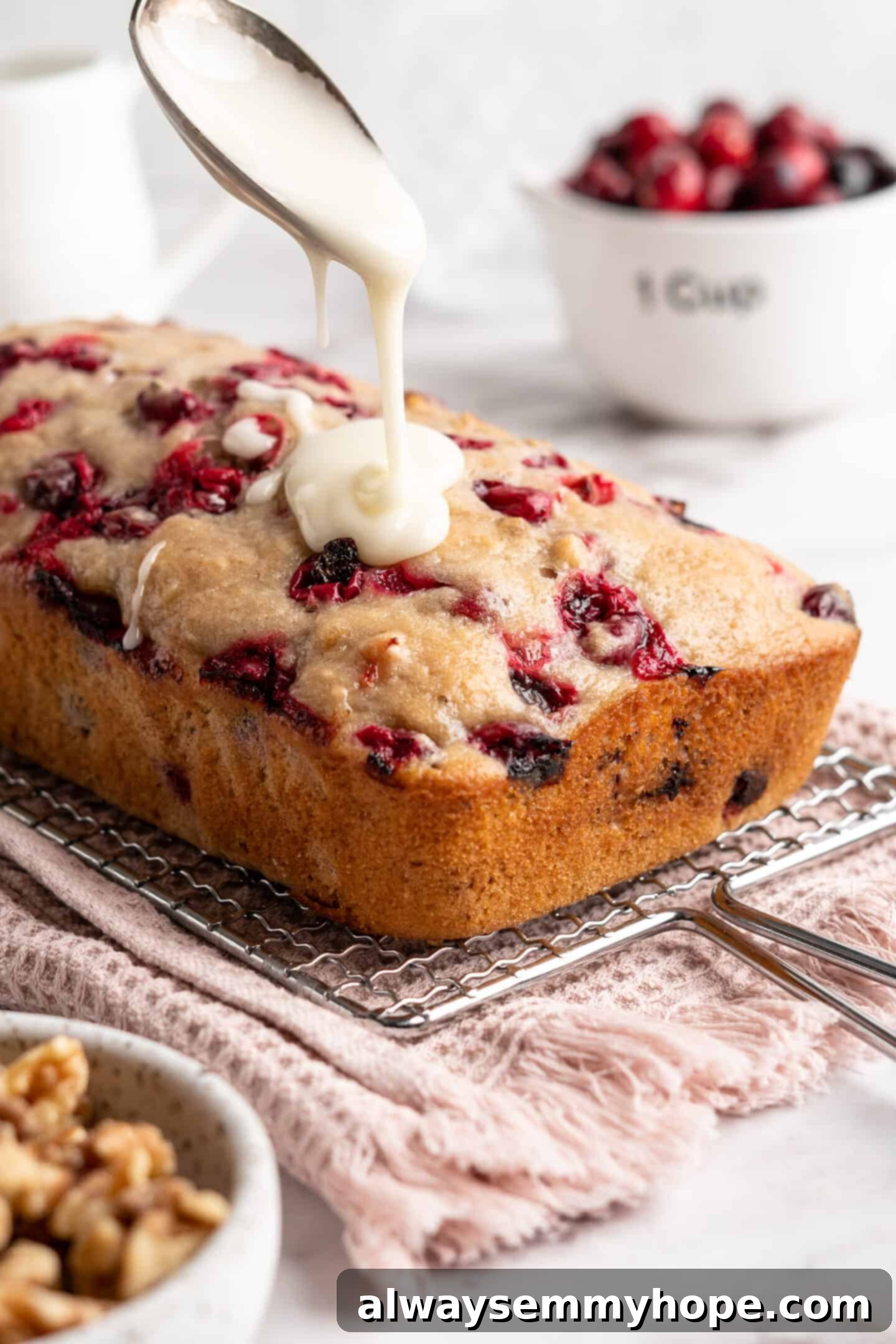 This moist cranberry walnut bread has just the right balance of sweetness, nuttiness, and tartness, and is a perfect holiday treat. A freshly baked loaf of cranberry walnut bread on a cooling rack, with a vibrant orange glaze being expertly drizzled over its top surface.