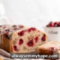 Bright Cranberry Orange Loaf with Citrus Glaze 2 A loaf of cranberry walnut bread on a cooling rack, sliced into, with a slice of bread in front of it and a bowl of cranberries behind it