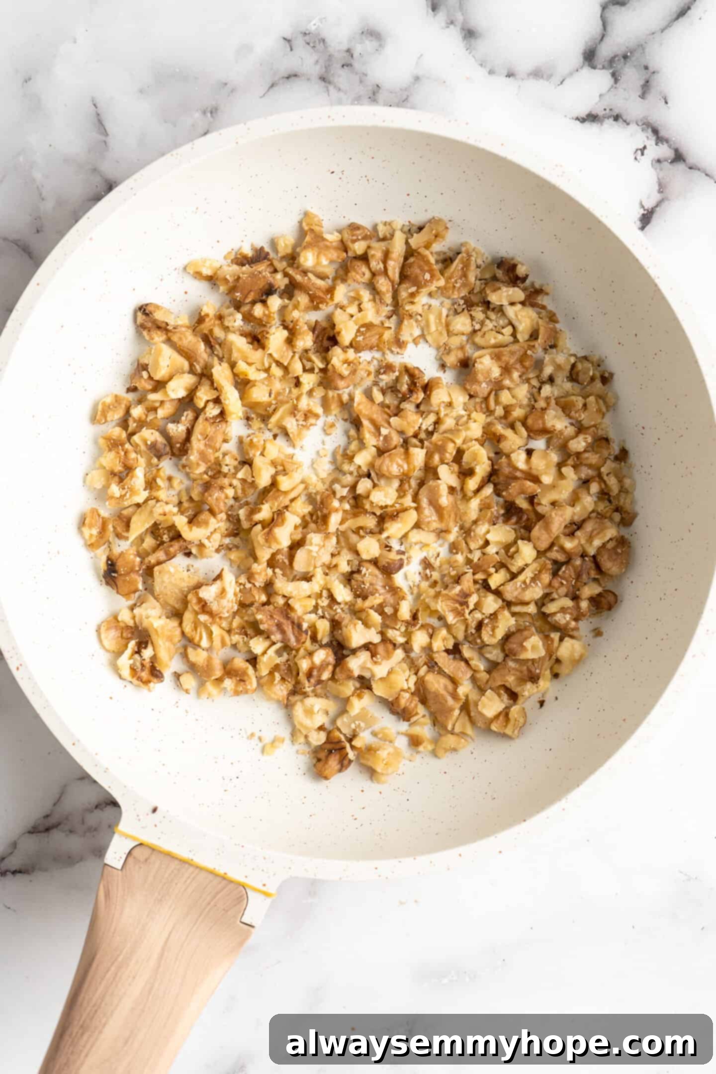 This moist cranberry walnut bread has just the right balance of sweetness, nuttiness, and tartness, and is a perfect holiday treat. A frying pan filled with lightly toasted walnuts, showcasing their golden-brown hue and ready for incorporation into the bread batter.