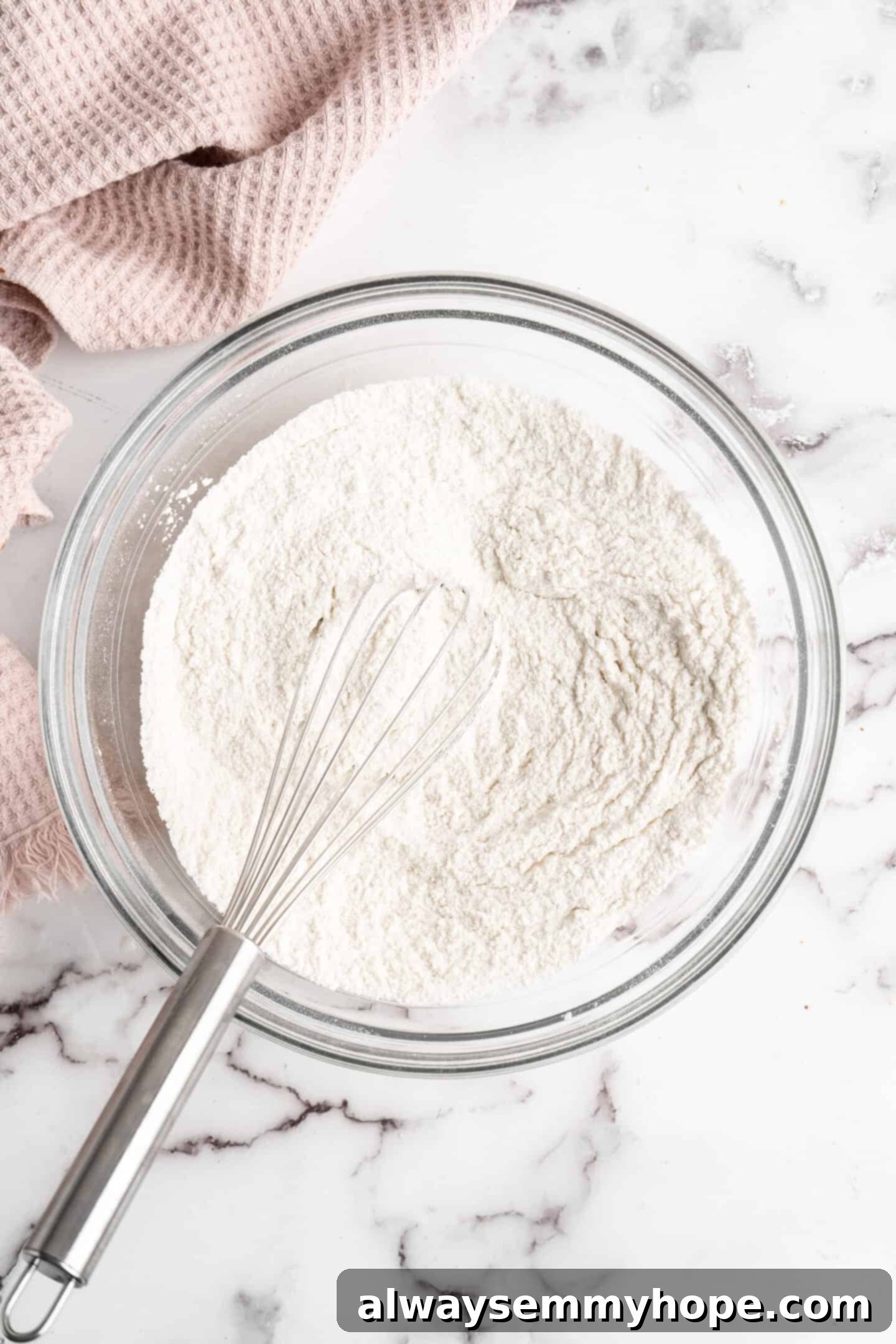 This moist cranberry walnut bread has just the right balance of sweetness, nuttiness, and tartness, and is a perfect holiday treat. A large mixing bowl containing a well-combined mixture of flour and sugar, with a whisk resting inside, ready for the wet ingredients.