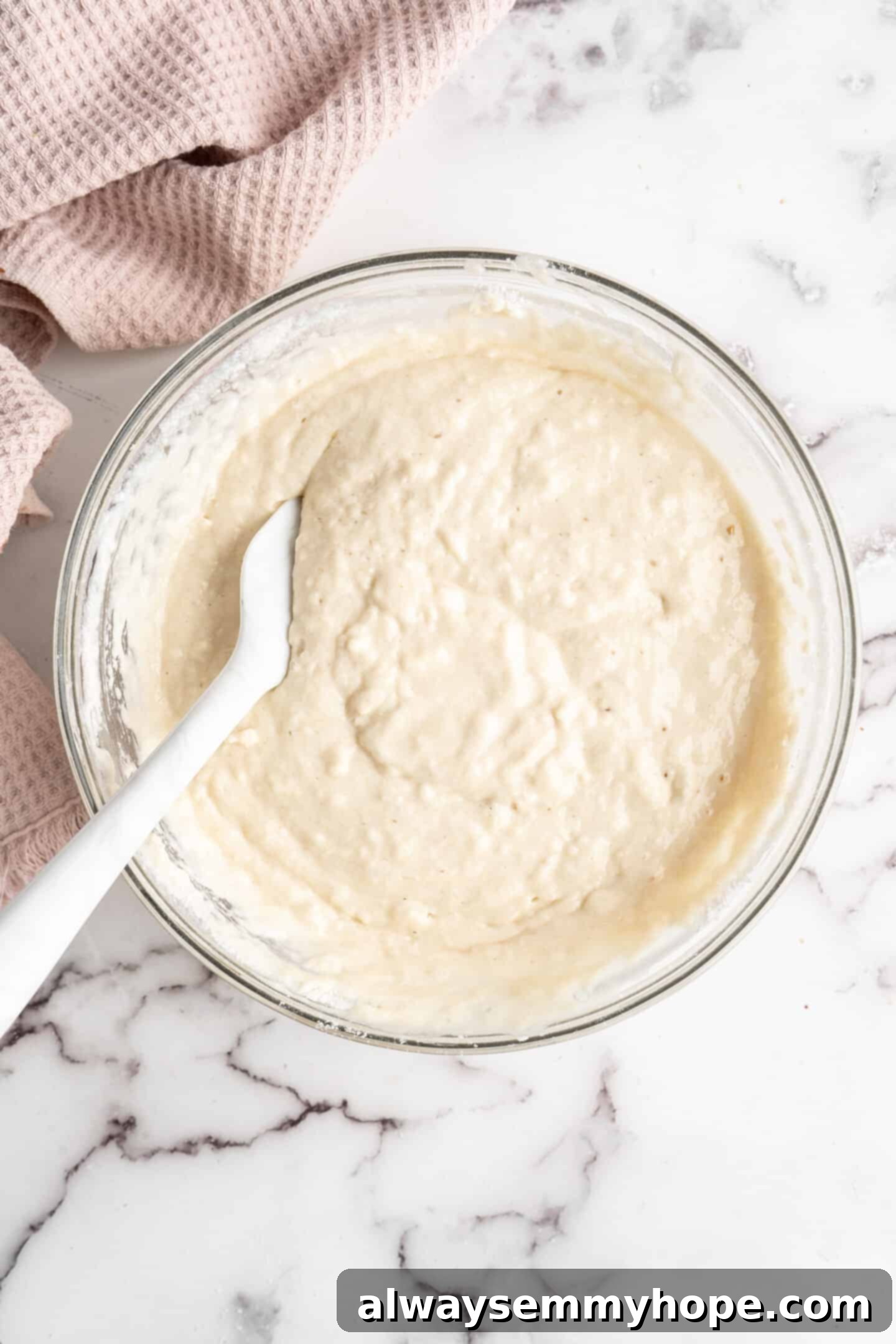 This moist cranberry walnut bread has just the right balance of sweetness, nuttiness, and tartness, and is a perfect holiday treat. A mixing bowl showcasing the fully combined wet and dry ingredients for cranberry walnut bread, forming a smooth batter, with a spatula resting inside.