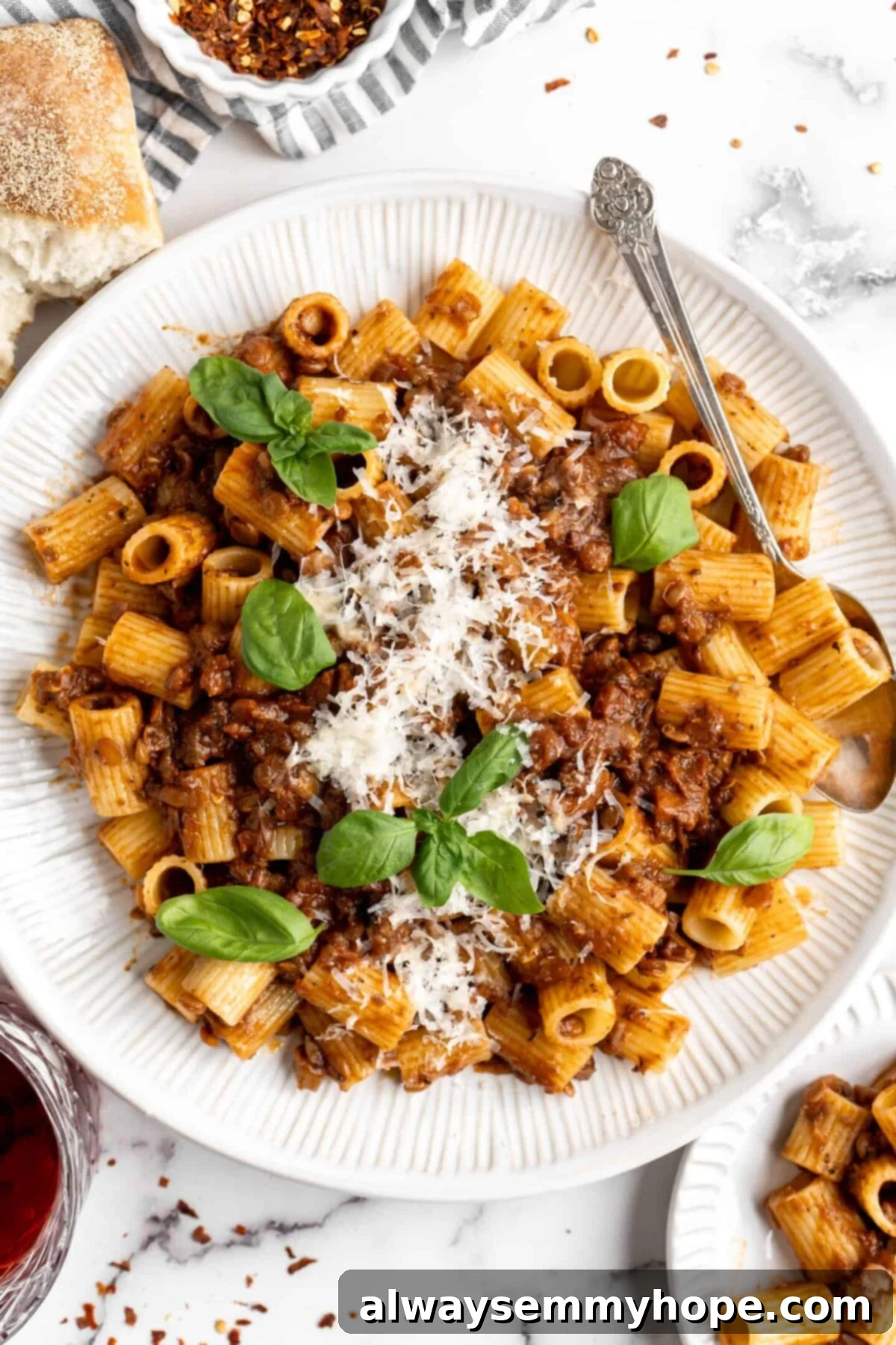 This easy walnut lentil bolognese recipe is a fun vegan take on a popular Italian pasta dish, and is full of tomato paste and veggies, creating a hearty and flavorful sauce. Overhead view of a plate of delicious vegan walnut lentil bolognese, garnished with fresh basil leaves and a sprinkle of vegan parmesan, with a fork ready to enjoy.