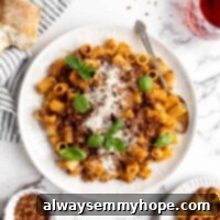 Hearty Walnut Lentil Ragu 2 A plate of walnut lentil bolognese, topped with basil and vegan parmesan, with a fork on the plate, next to plates of pasta, a baguette, and a bowl of chili flakes
