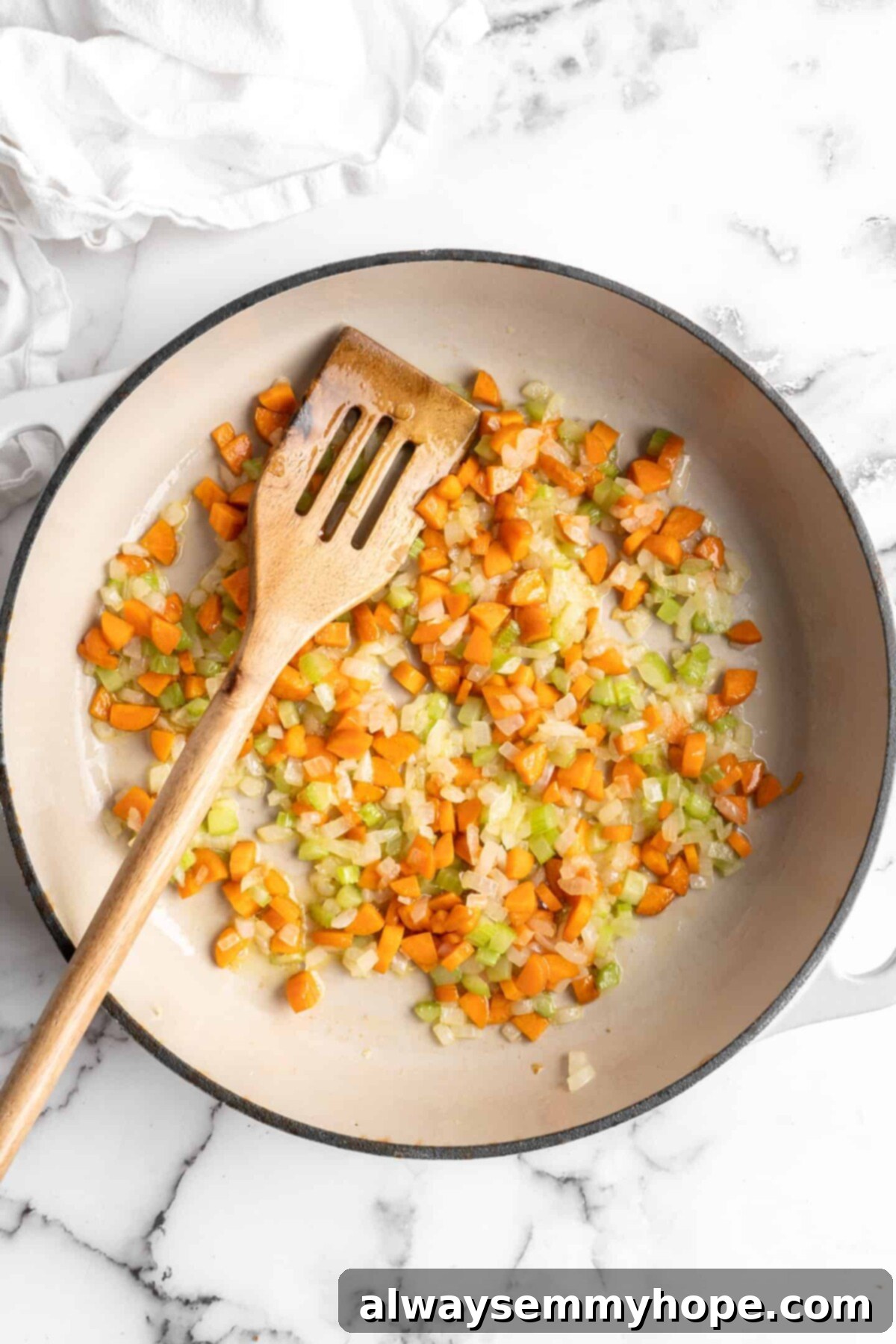 This easy walnut lentil bolognese recipe is a fun vegan take on a popular Italian pasta dish, and is full of tomato paste and veggies, showcasing the initial cooking of aromatics. A pan with onions, celery, and carrots cooking in it, with a wooden spoon in the pan, forming the aromatic base of the bolognese.
