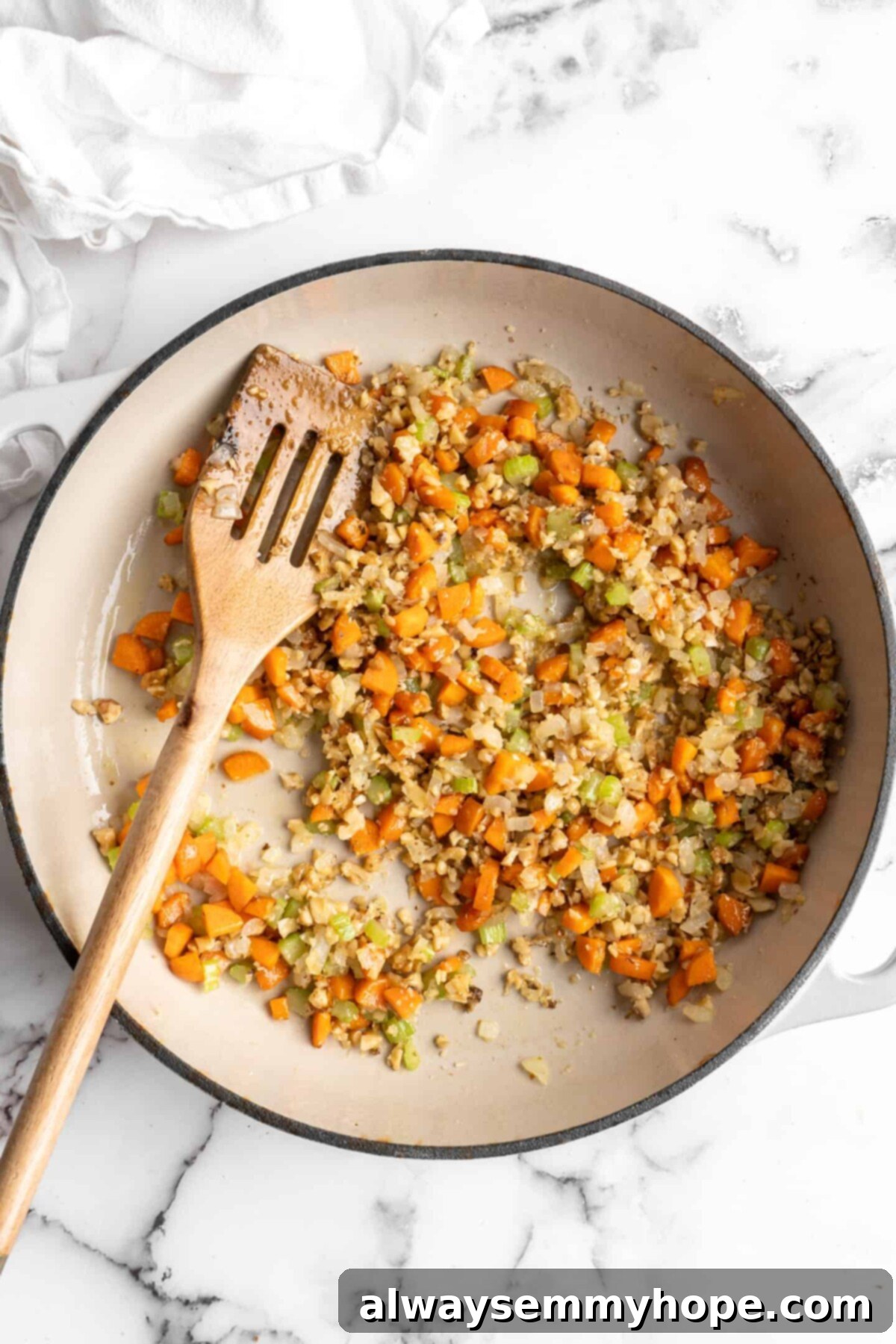 This easy walnut lentil bolognese recipe is a fun vegan take on a popular Italian pasta dish, and is full of tomato paste and veggies, highlighting the nutty addition. A pan with onions, carrots, celery, walnuts, and a wooden spoon in it, illustrating the addition of walnuts to the soffritto base.