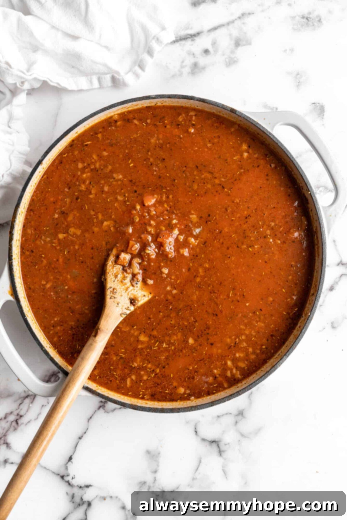 This easy walnut lentil bolognese recipe is a fun vegan take on a popular Italian pasta dish, and is full of tomato paste and veggies, illustrating the sauce in early stages. A pot with walnut lentil bolognese cooking in it, with lots of broth, before thickening.