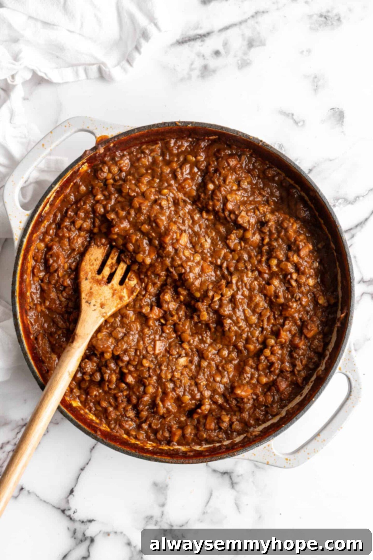 This easy walnut lentil bolognese recipe is a fun vegan take on a popular Italian pasta dish, and is full of tomato paste and veggies, showing the final sauce texture. A pot of finished, thickened walnut lentil bolognese sauce, with a wooden spoon, ready to be served.