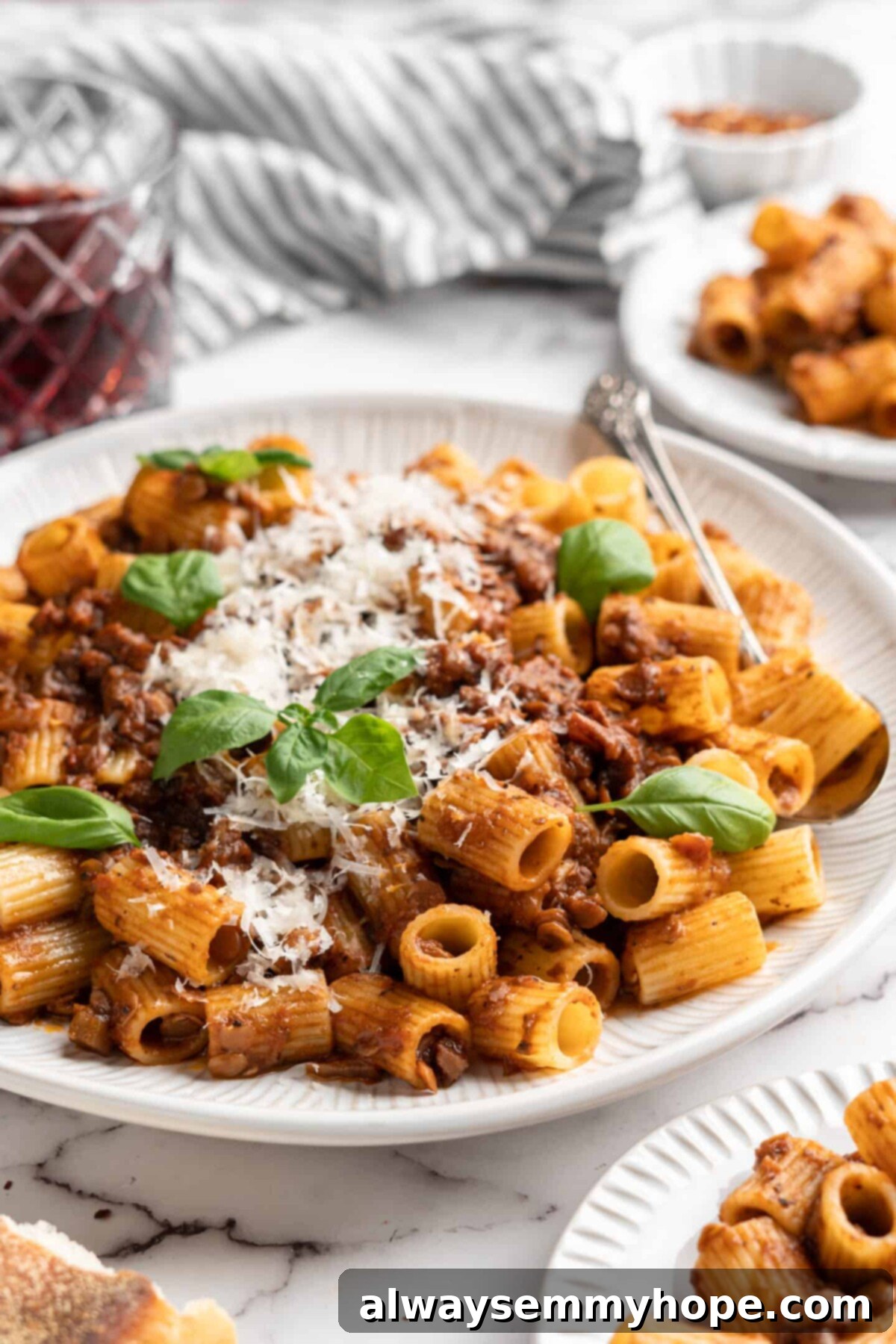 This easy walnut lentil bolognese recipe is a fun vegan take on a popular Italian pasta dish, and is full of tomato paste and veggies, presented as a finished dish. A plate of perfectly plated vegan walnut lentil bolognese, generously topped with vegan cheese and fresh basil, ready to be enjoyed.