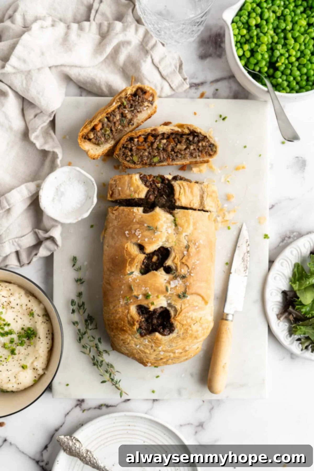 This vegan wellington recipe uses mushrooms, walnuts, and vegan beef to replace meat. It's a hearty holiday meal that's easy to make. A beautifully baked vegan wellington loaf, expertly sliced to reveal its rich, savory filling of plant-based beef, mushrooms, and walnuts. Two perfect slices rest on a wooden cutting board beside a paring knife and fresh thyme sprigs, with a side of creamy mashed potatoes in the background. This hearty and elegant plant-based dish is perfect for festive occasions.