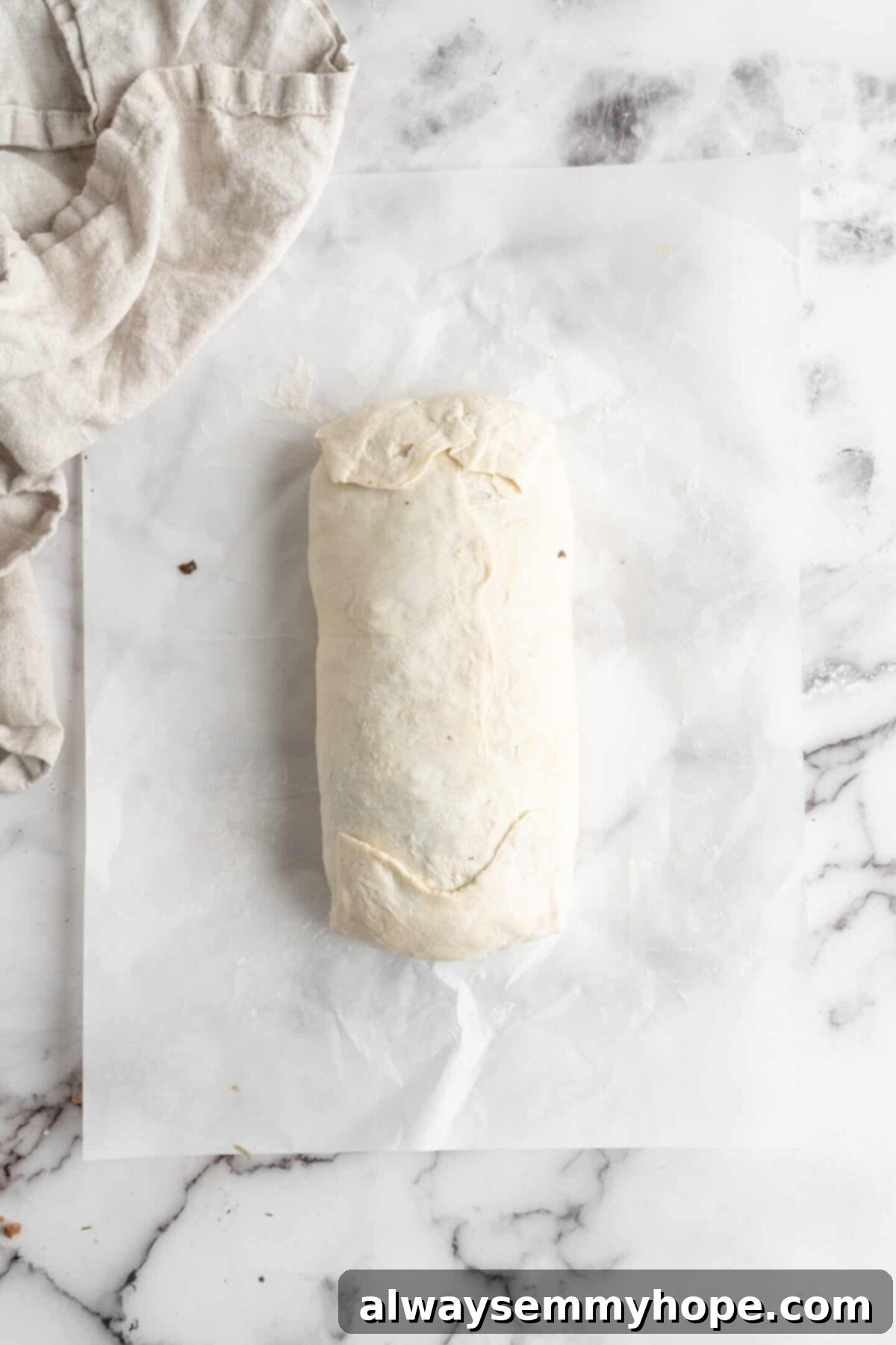 This vegan wellington recipe uses mushrooms, walnuts, and vegan beef to replace meat. It's a hearty holiday meal that's easy to make. An assembled vegan wellington, perfectly wrapped and sealed, resting on a piece of parchment paper on a baking sheet, ready for scoring and baking.
