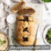 Plant-Based Wellington 2 A beautifully baked vegan wellington loaf, expertly sliced to reveal its rich, savory filling of plant-based beef, mushrooms, and walnuts. Two perfect slices rest on a wooden cutting board beside a paring knife and fresh thyme sprigs, with a side of creamy mashed potatoes in the background. This hearty and elegant plant-based dish is perfect for festive occasions.