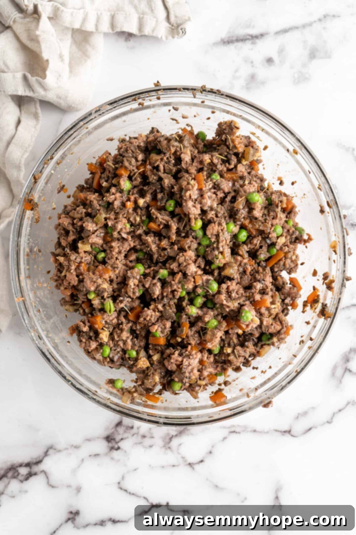 This vegan wellington recipe uses mushrooms, walnuts, and vegan beef to replace meat. It's a hearty holiday meal that's easy to make. A mixing bowl filled with a fully combined vegan wellington filling, showcasing the vibrant colors of peas and carrots interspersed within the savory vegan beef, mushroom, and walnut mixture, indicating readiness for assembly.