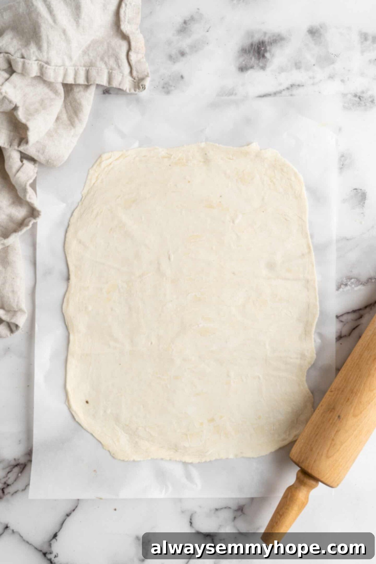 This vegan wellington recipe uses mushrooms, walnuts, and vegan beef to replace meat. It's a hearty holiday meal that's easy to make. A perfectly rolled rectangular sheet of golden puff pastry laid out on a clean surface, with a kitchen towel and a rolling pin nearby, ready for the wellington filling.