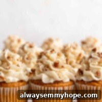 Three perfectly frosted vegan pumpkin cupcakes adorned with creamy vegan cream cheese and pecans, with a soft focus on more delightful cupcakes in the background.