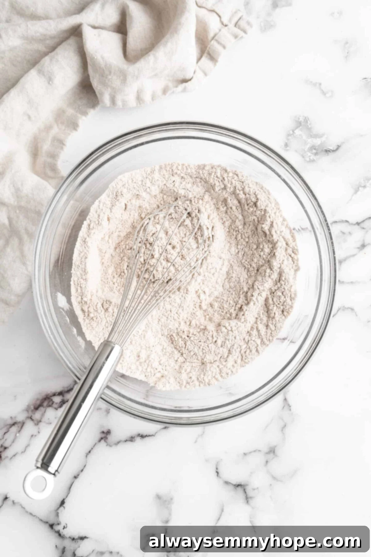 A mixing bowl filled with a perfectly combined flour mixture, with a whisk resting inside, ready for the next step of the recipe.