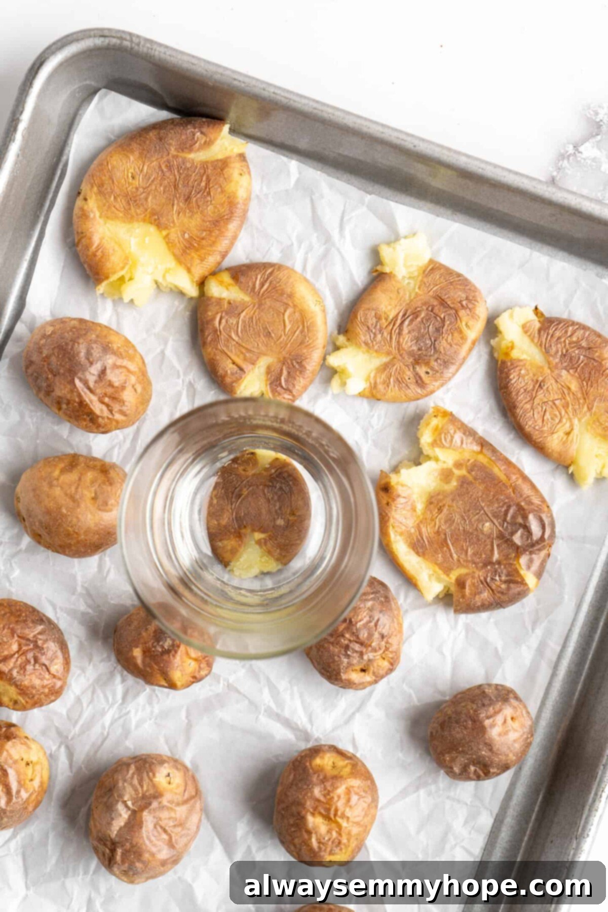 This air fryer smashed potatoes recipe is salty, crispy on the outside, and light and fluffy on the inside. It's an easy side dish, and vegan! A baking sheet with cooked potatoes and smashed potatoes, with a drinking glass on top of one of the smashed potatoes