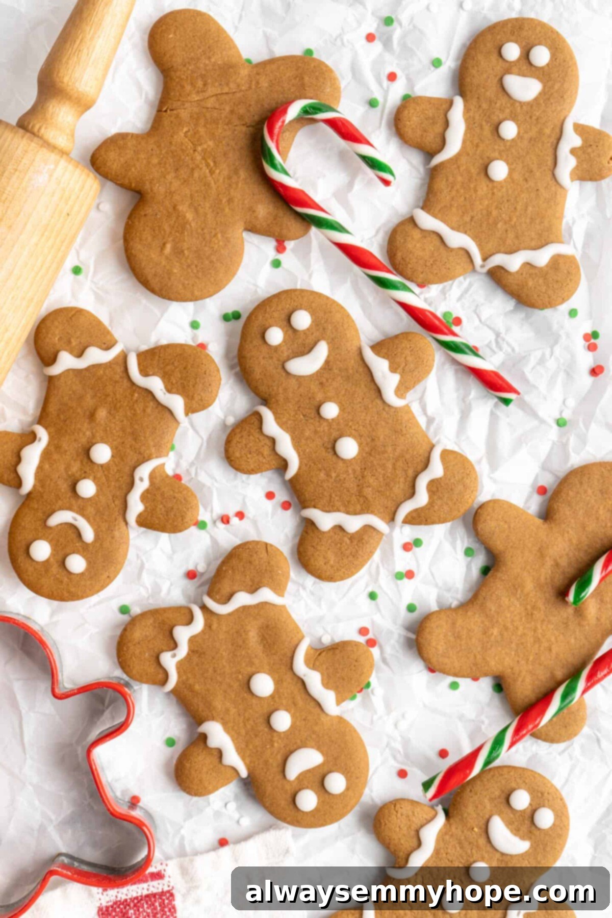 A few decorated gingerbread men next to a few undecorated gingerbread men, surrounded by candy canes and a rolling pin