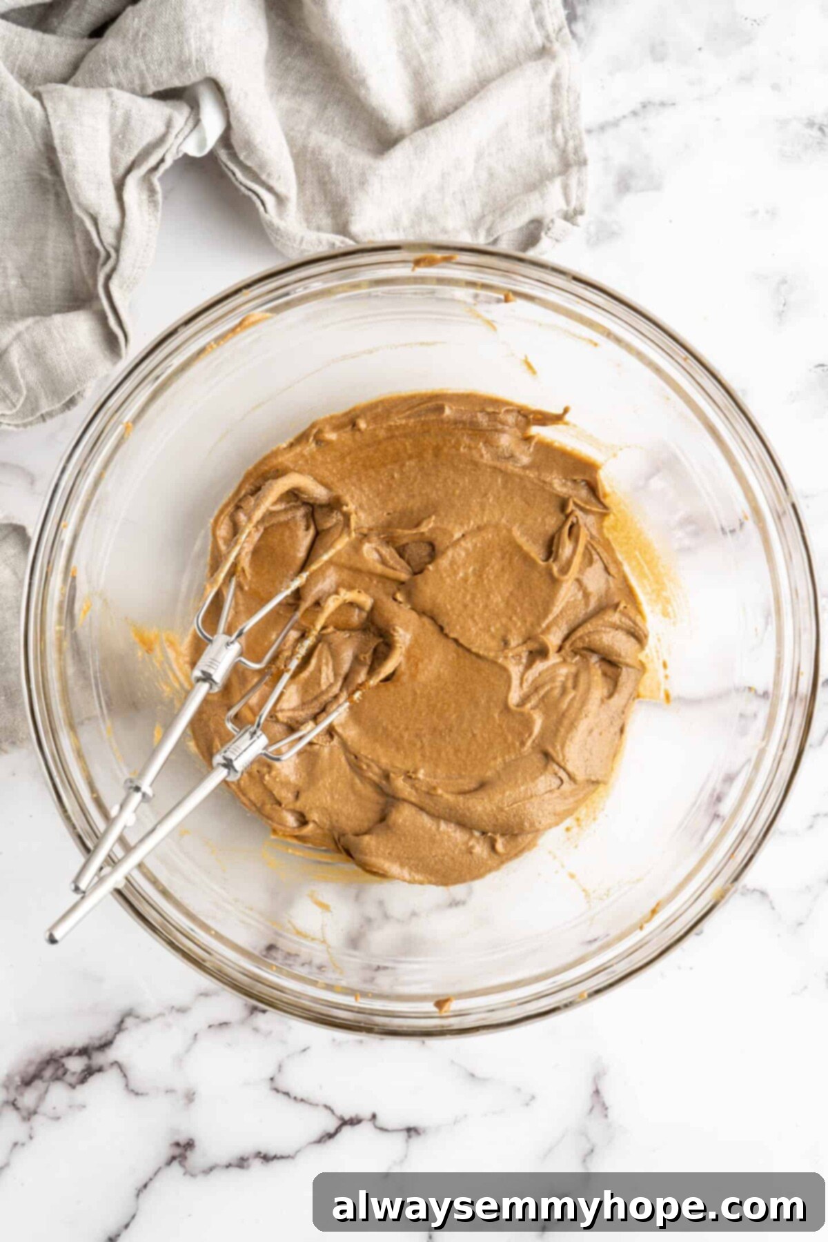 A glass bowl with the wet ingredients for gingerbread men mixed together, with two electric beater blades in the bowl